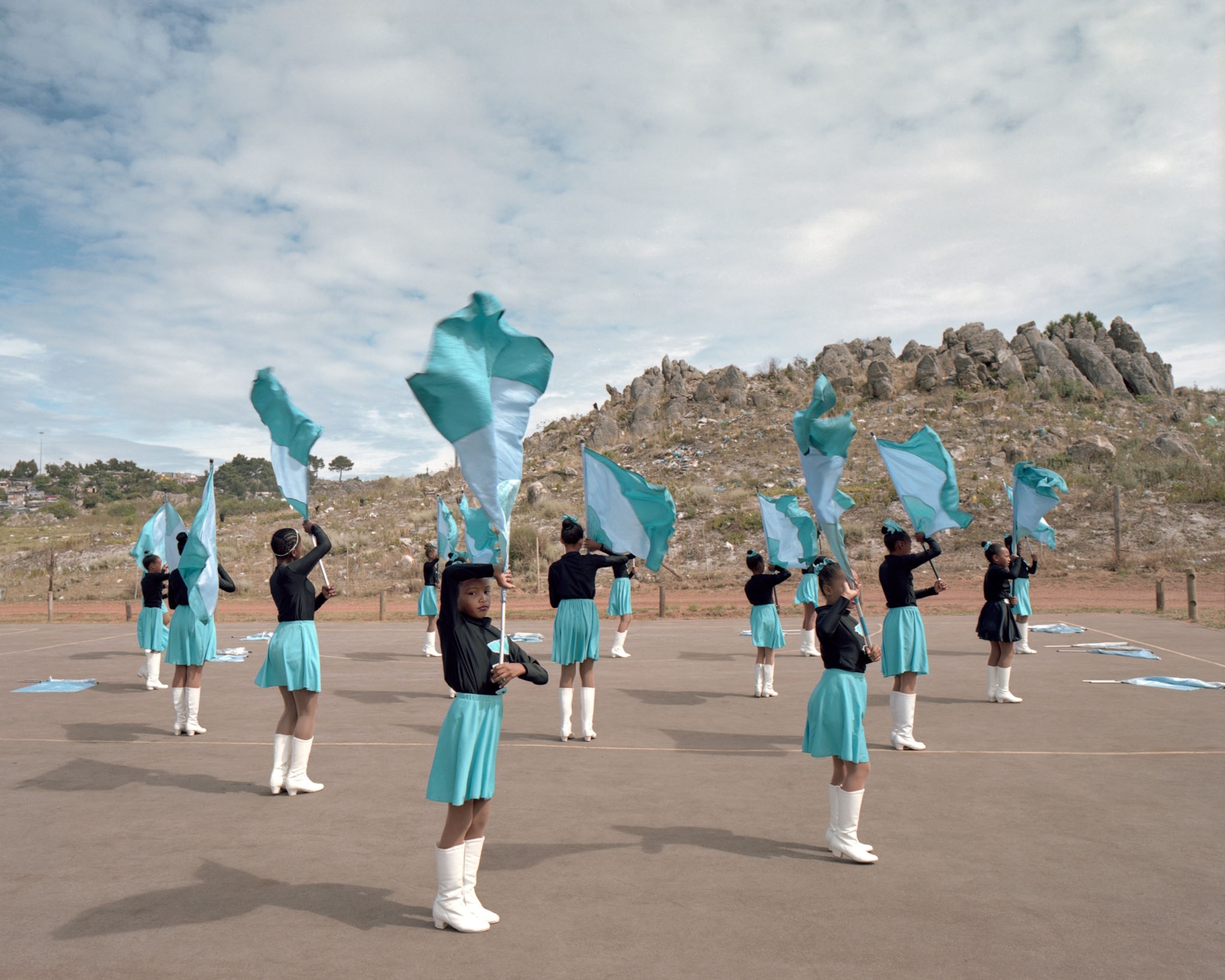 young women in teal and black uniforms twirling flags outside