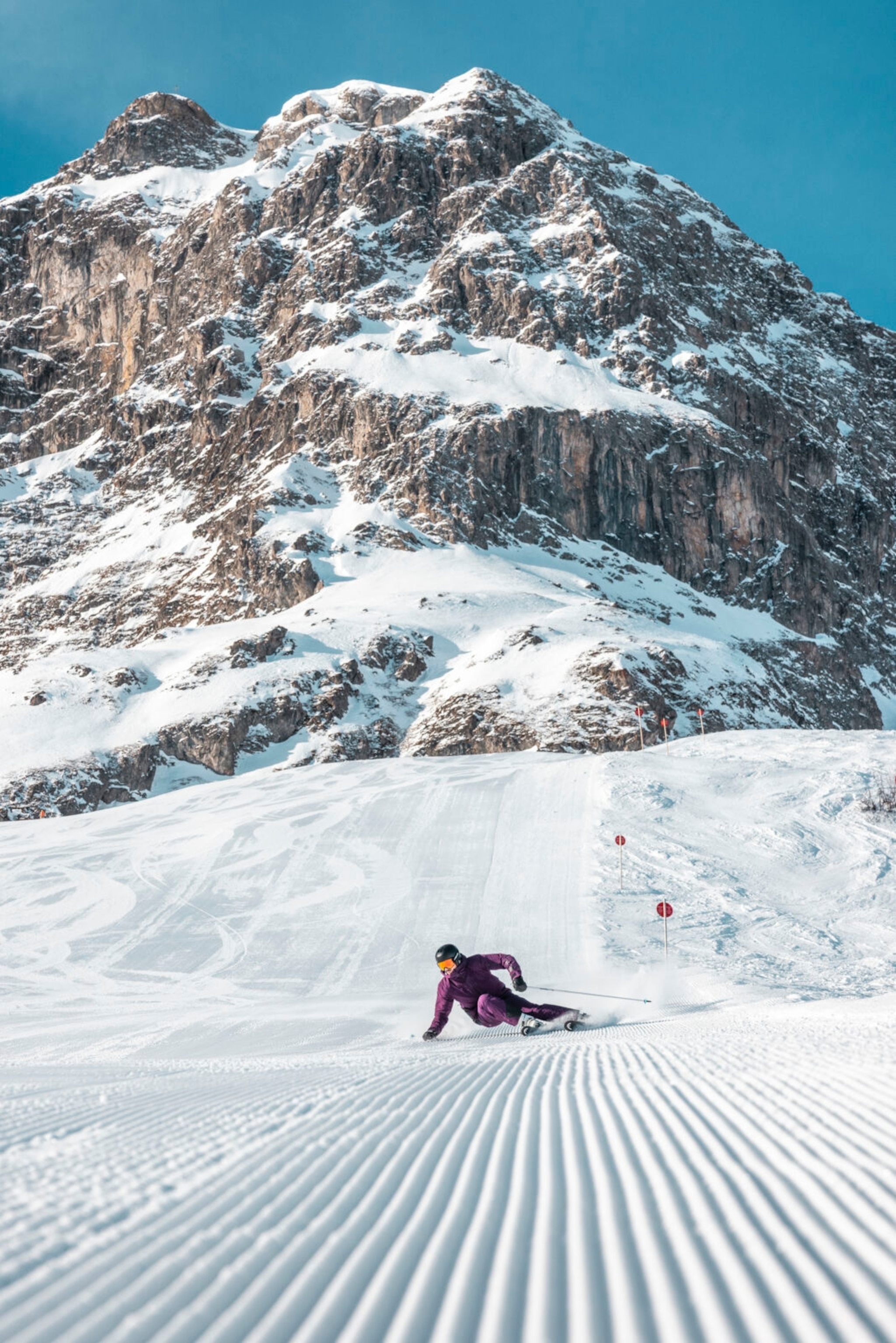 A skiier going down a fresh piste with impressive snow-capped mountains in the background.