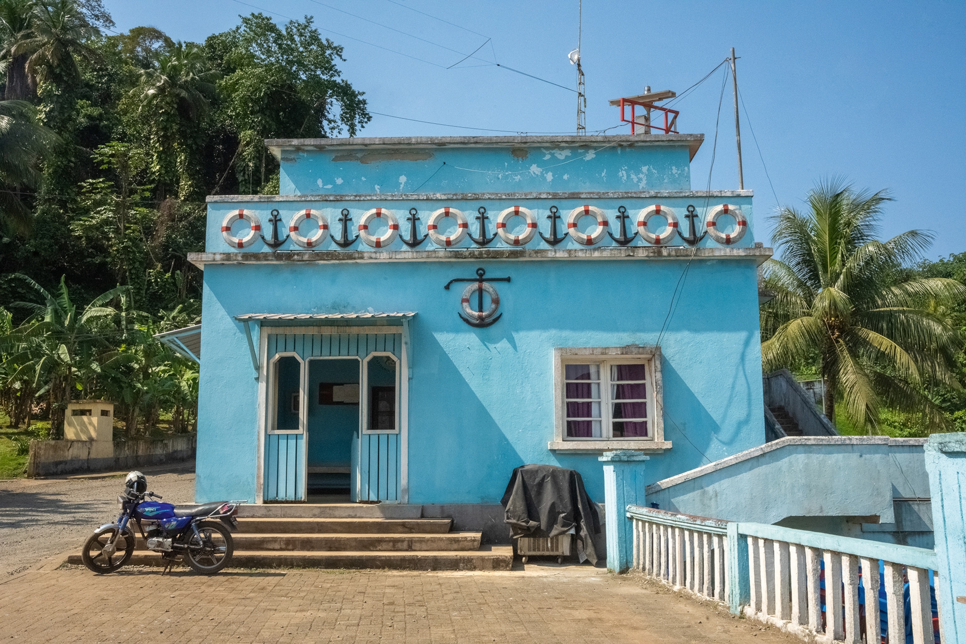 A limestone house with arched door features and anchors adorning the front wall as a motorbike is parked outside.