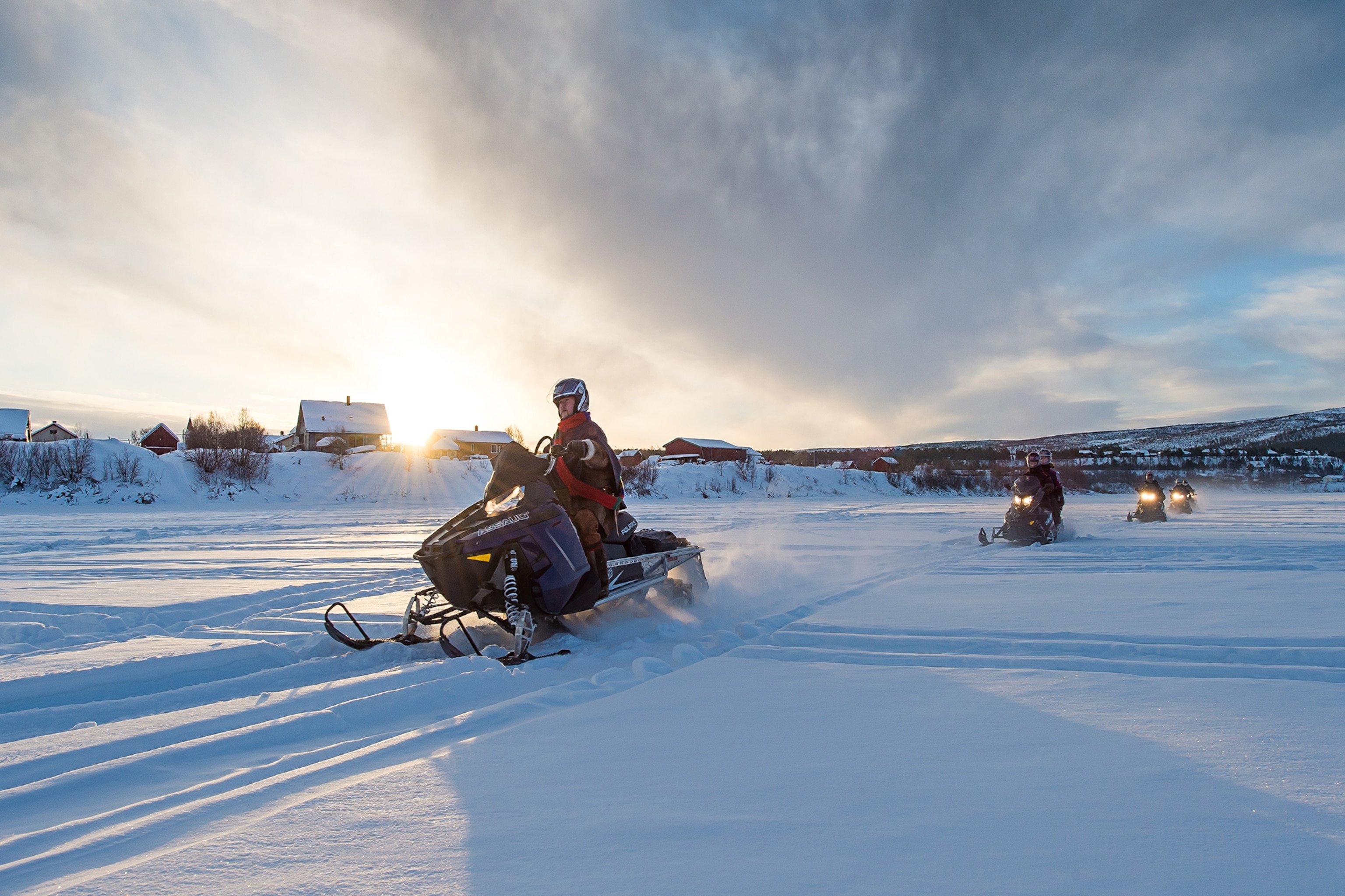 Several snowmobilers travel across the snow as the sun sets in Karasjok.