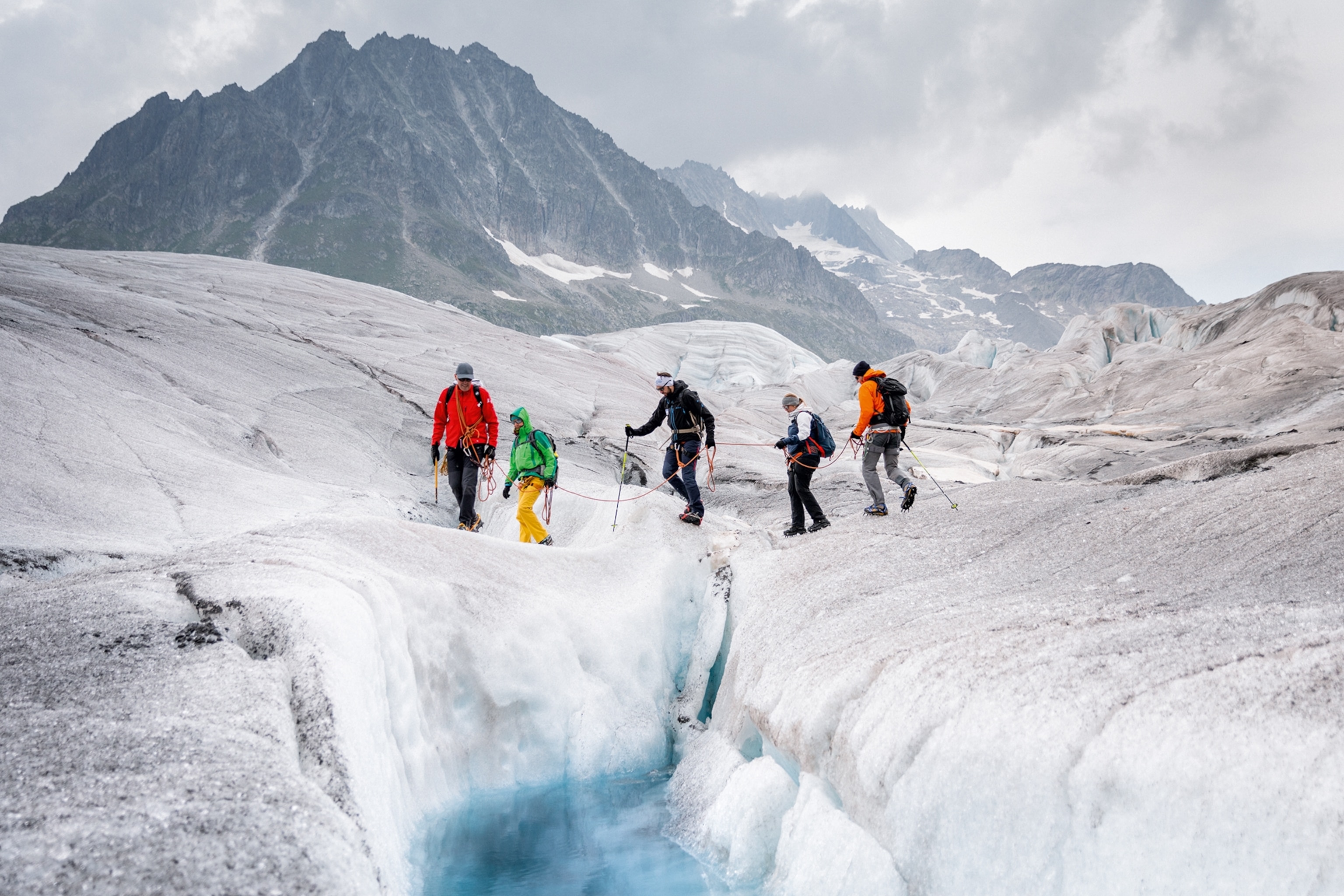Travellers connected by rope walk past a crevice of the Great Aletsch Glacier, led by a mountain guide.