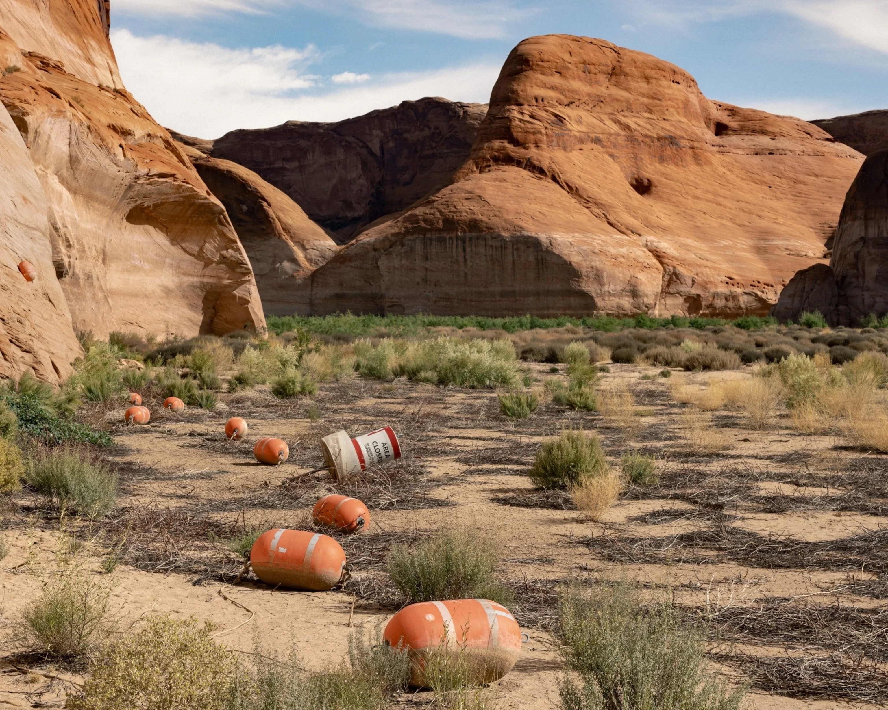 Orange buoys scattered on dry land between red rock formations under a blue sky