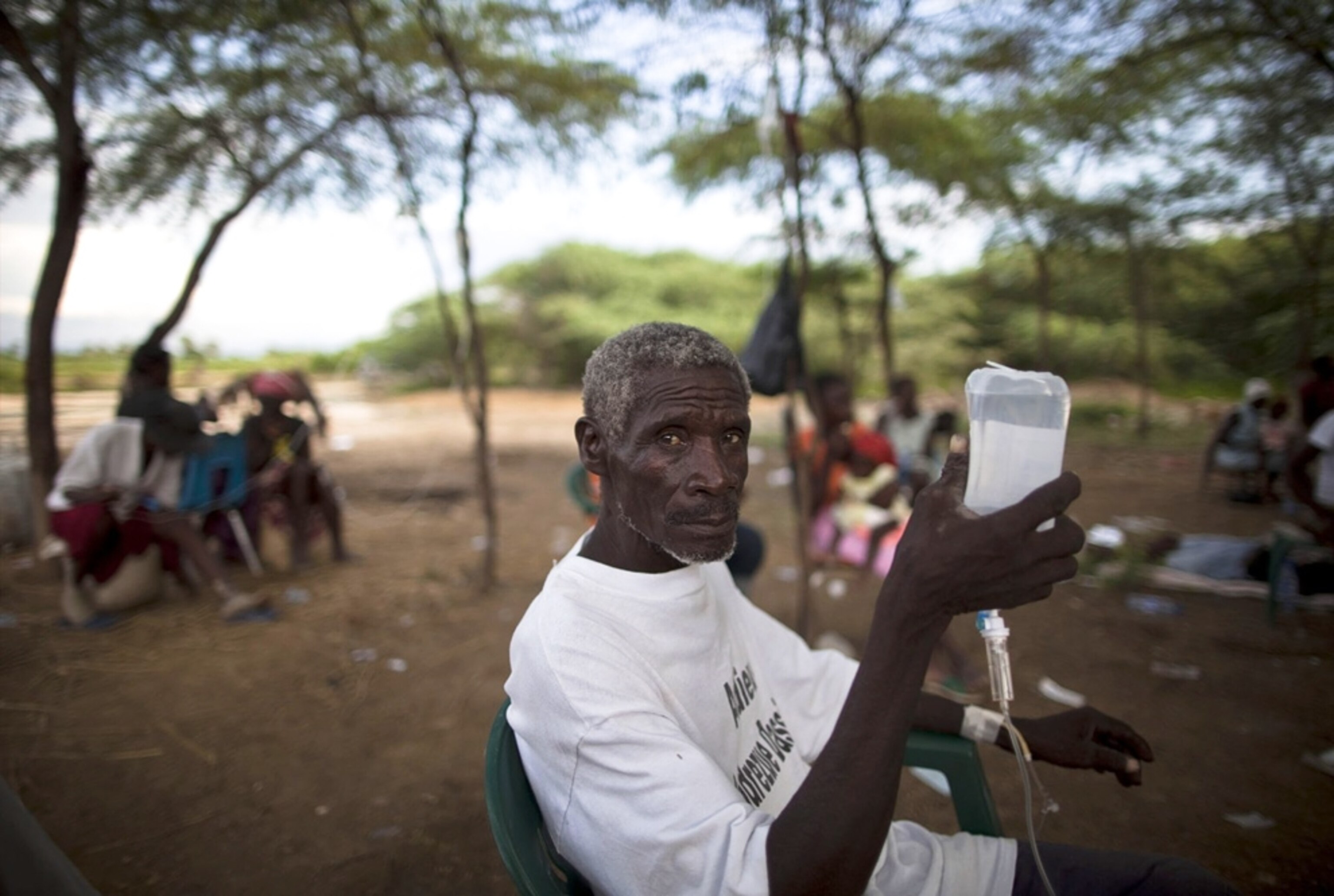 A cholera victim sits in a chair outside and holds his IV serum bag aloft -- picture from a photo gallery on the one-year Haiti-earthquake anniversary