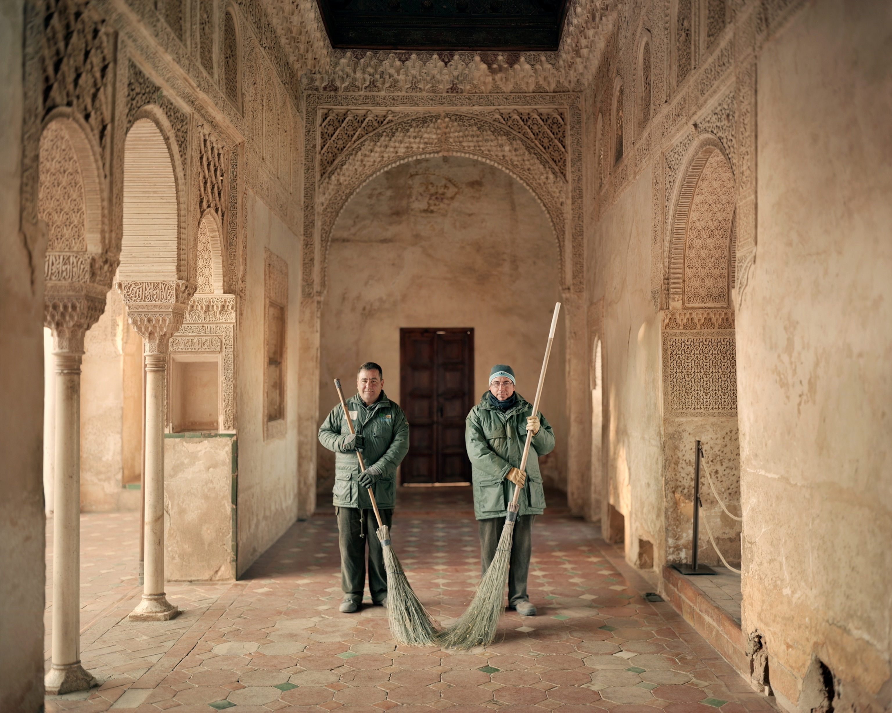 Two men with brooms in the arcade.