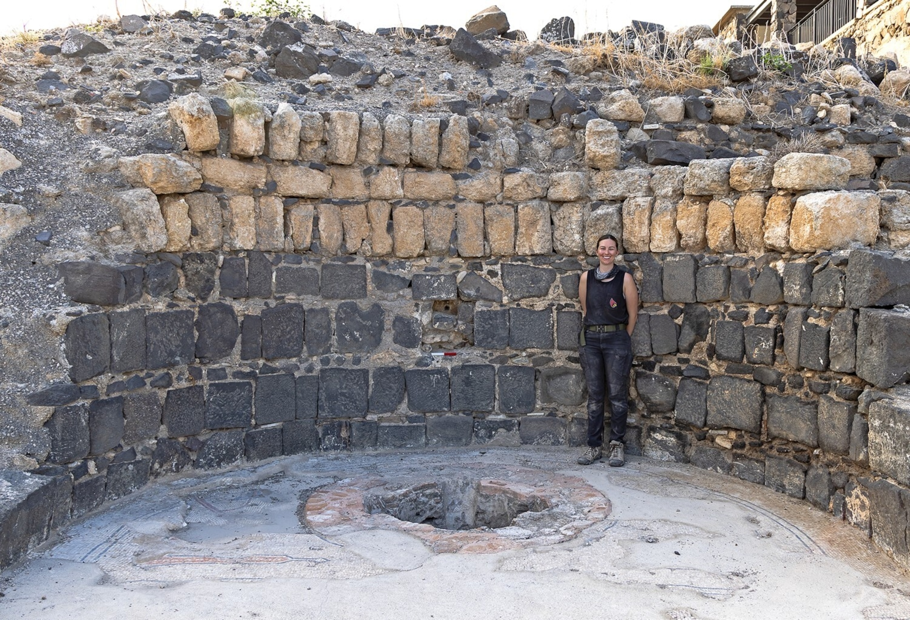 A woman stands surrounded by a recently excavated wall, formed from individual blocks