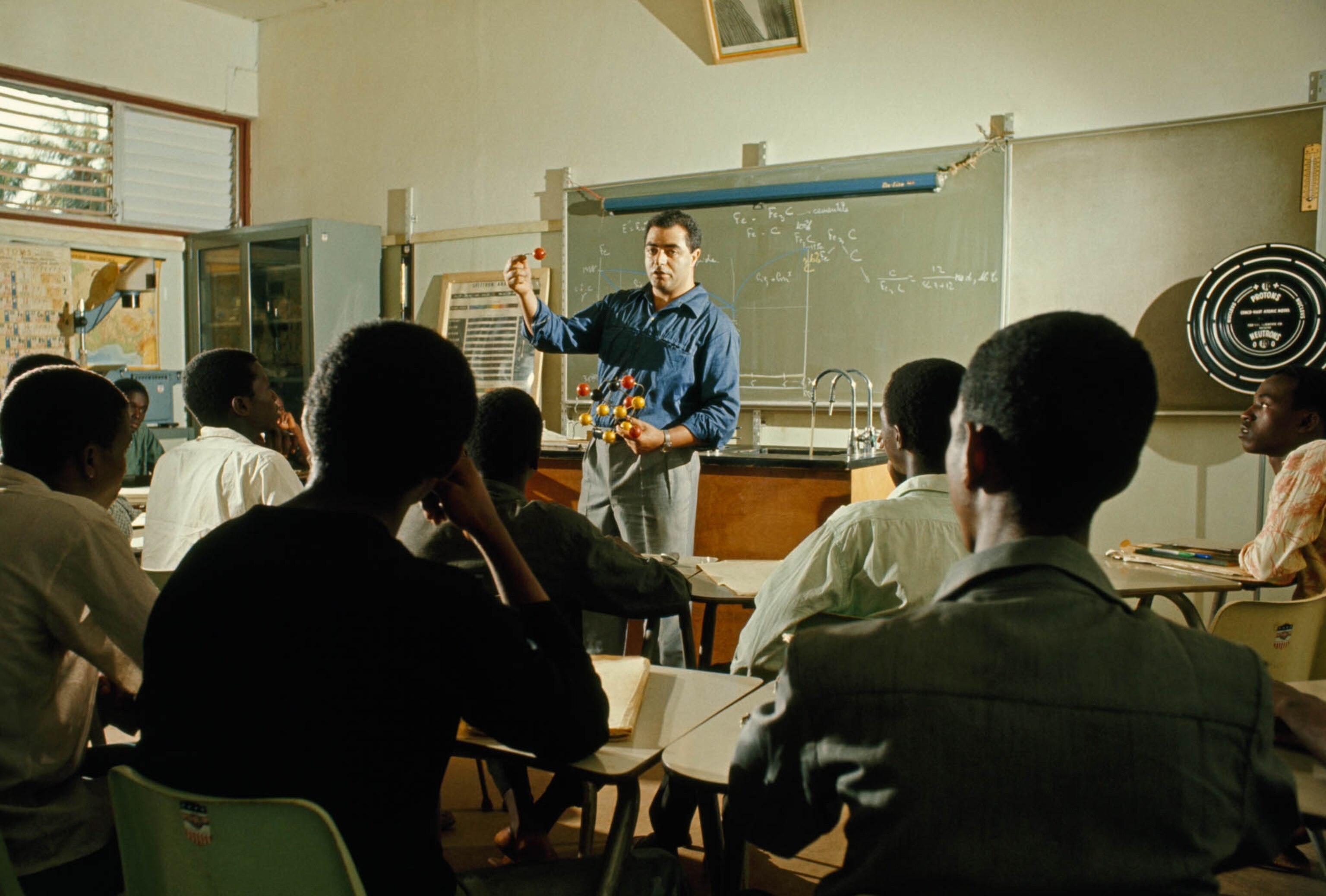 a teacher holding a model of an atom while teaching a class in Conakry, Guinea