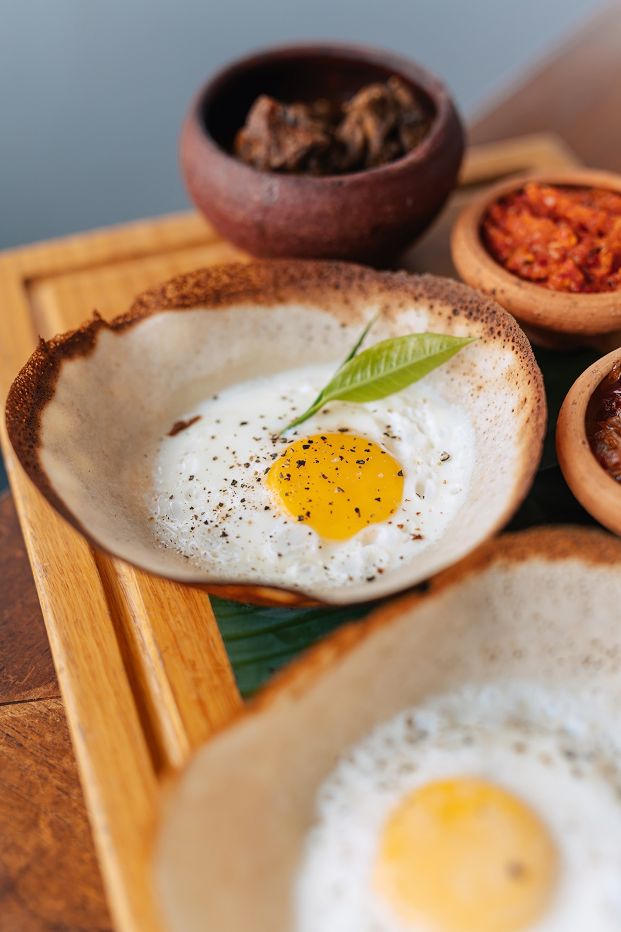 A close-up of a crisped and bowl-shaped pancake filled with a fried egg on a wooden platter.
