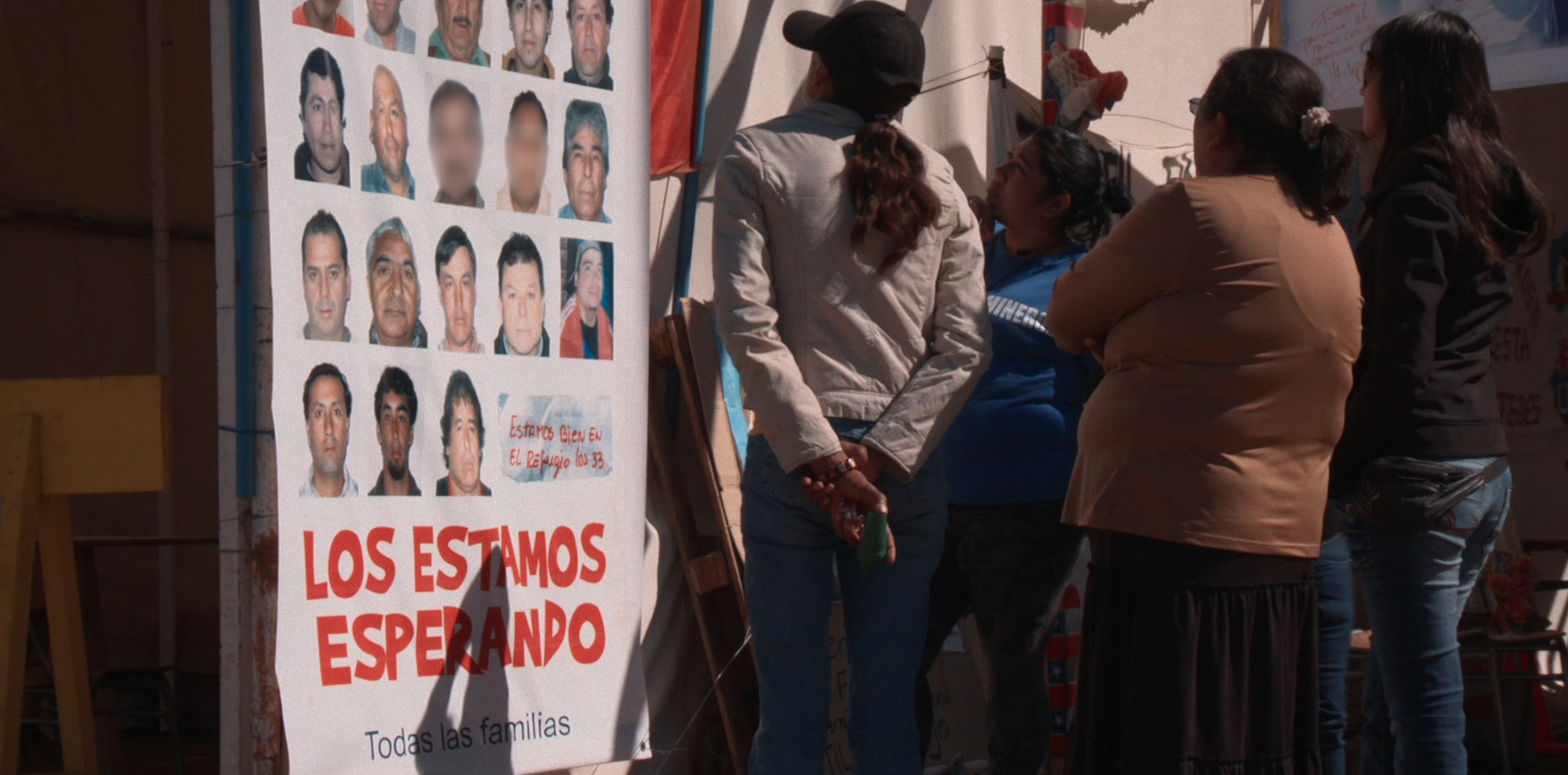 People stand and look at a poster showing photos of each of the missing miners faces