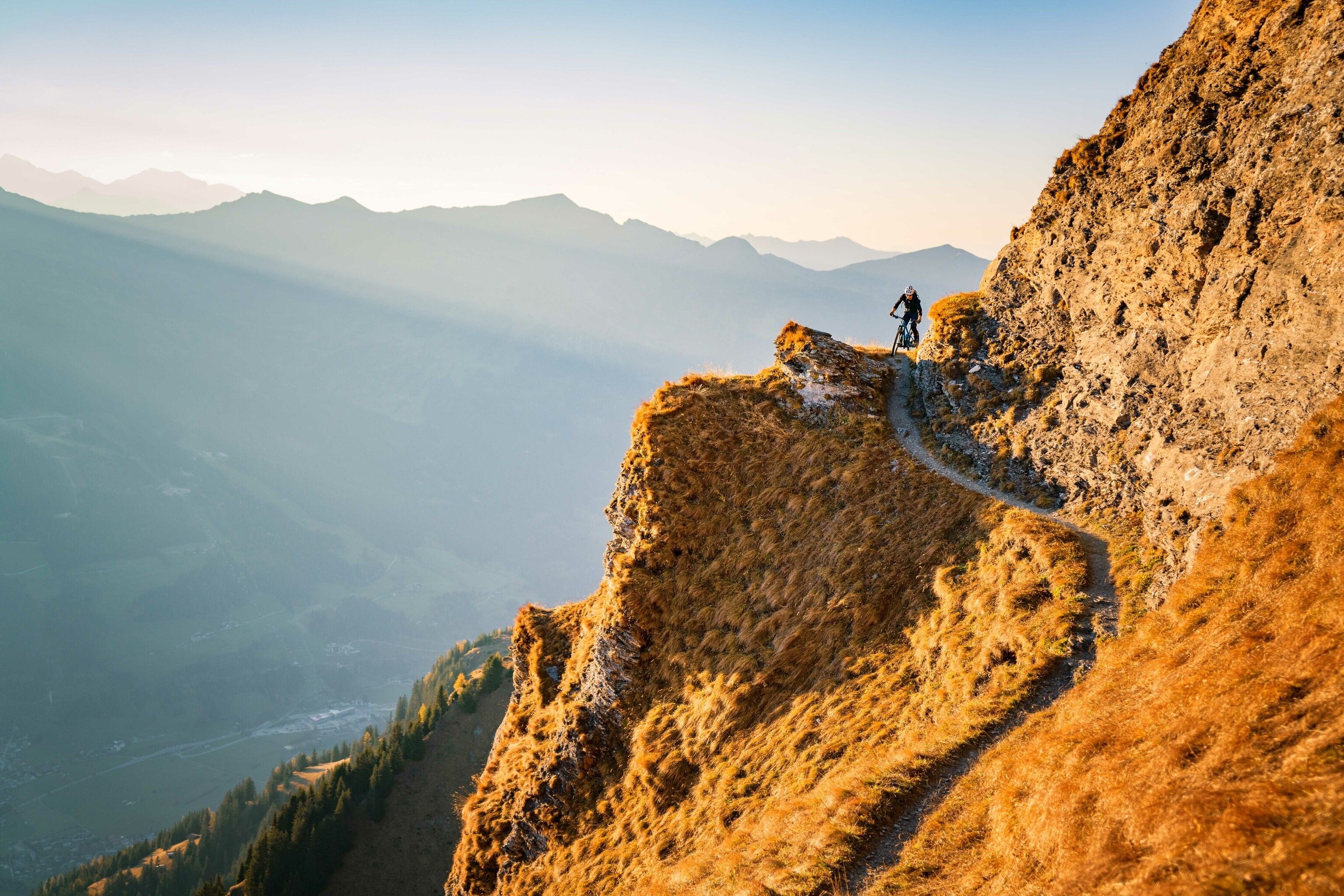 A cyclist traverses a narrow mountain path.