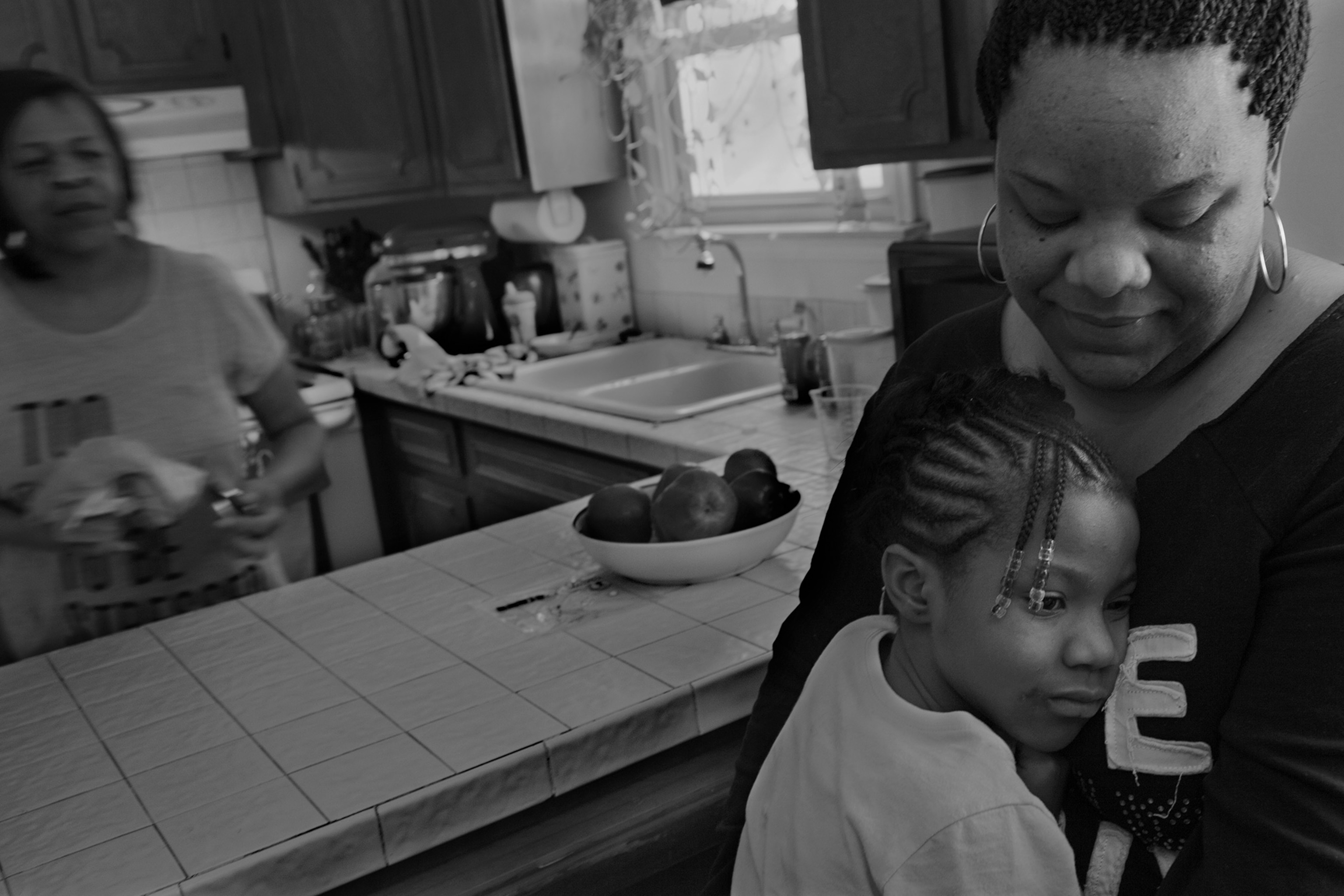 a young girl and woman embracing with another woman in the background