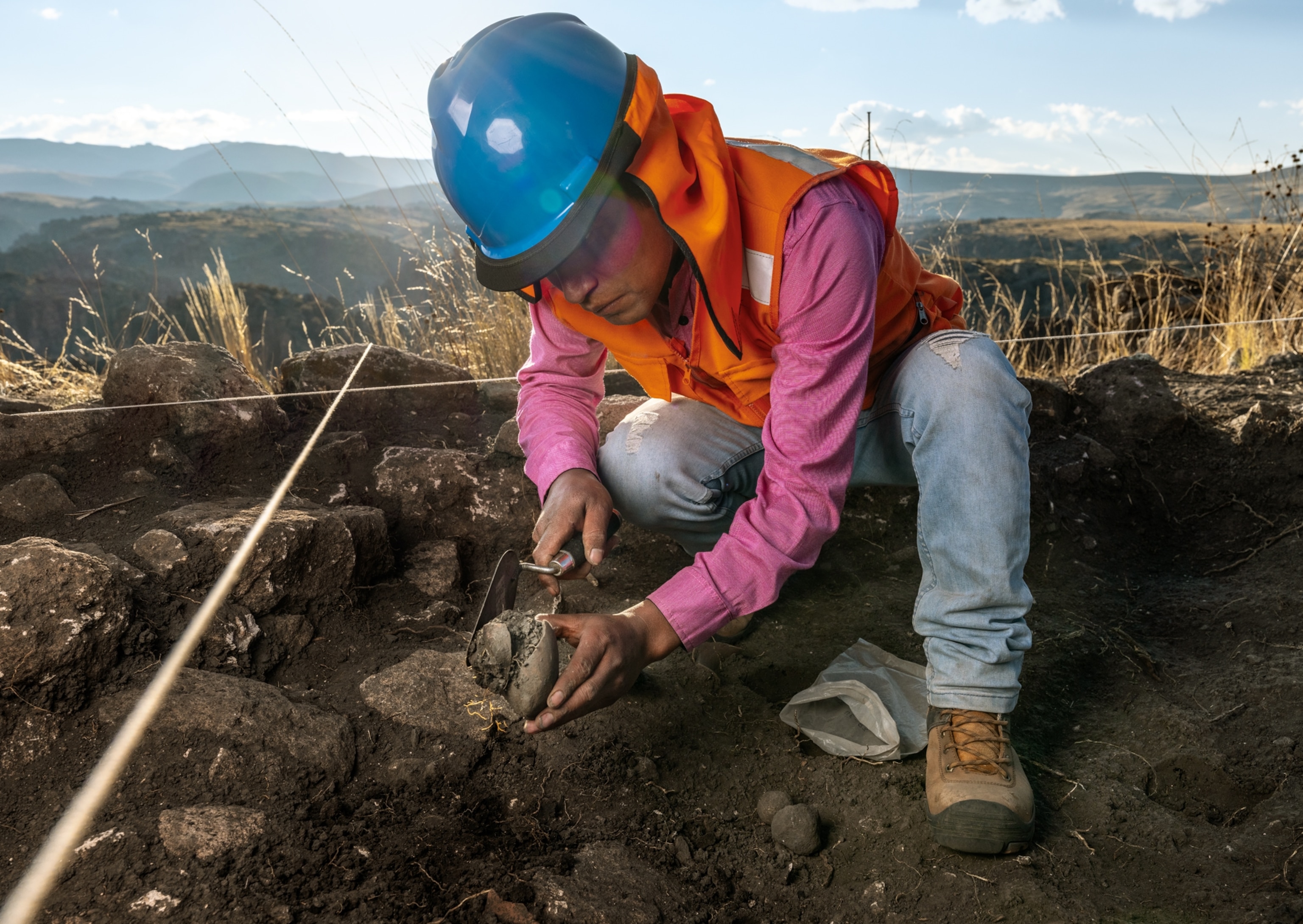Person in orange vest and blue hard hat holding an object he just excavated.