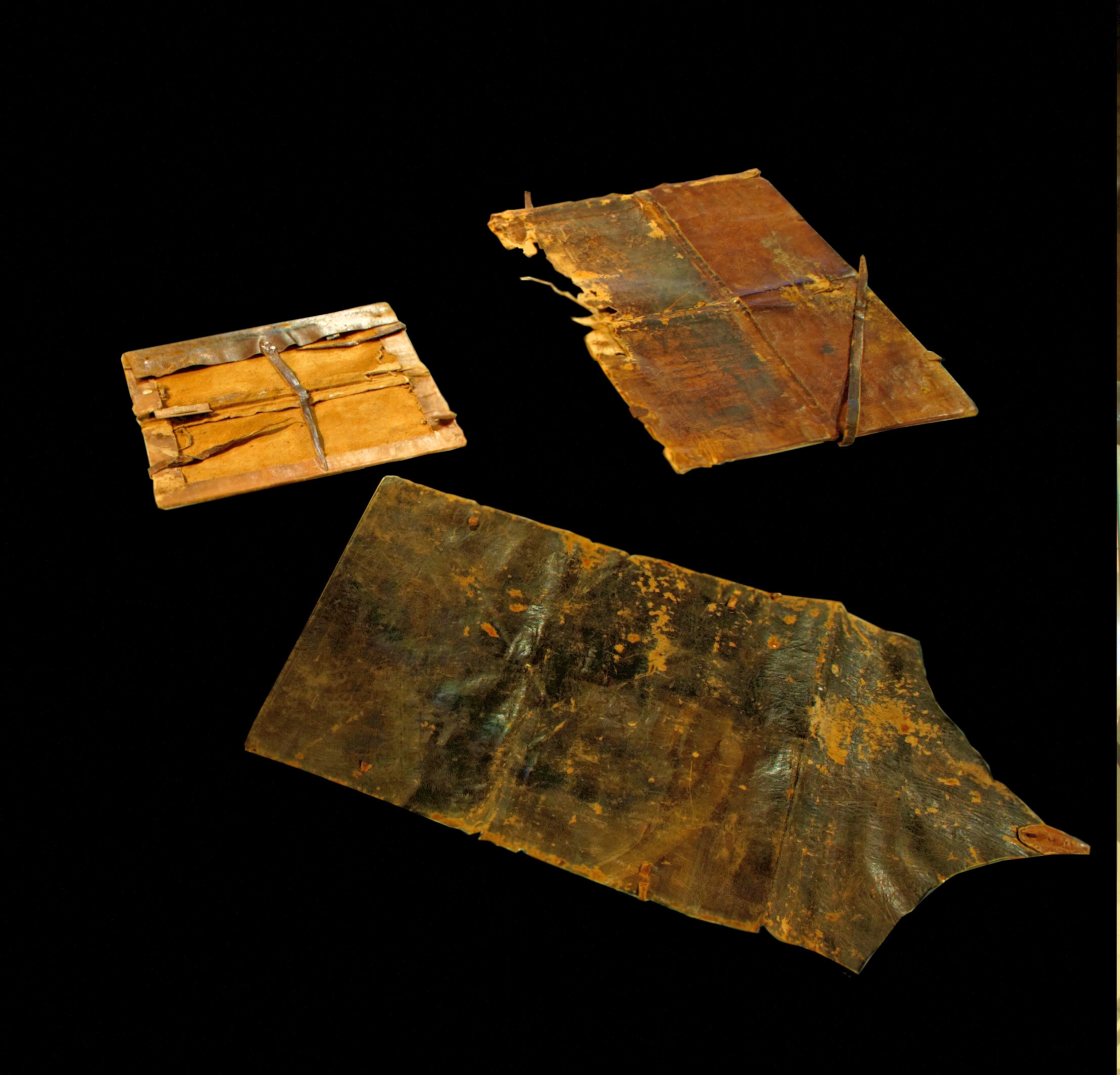 Aged, fragmented codex covers on a black background. The weathered leather surfaces are tinged with rich brown hues and golden textures