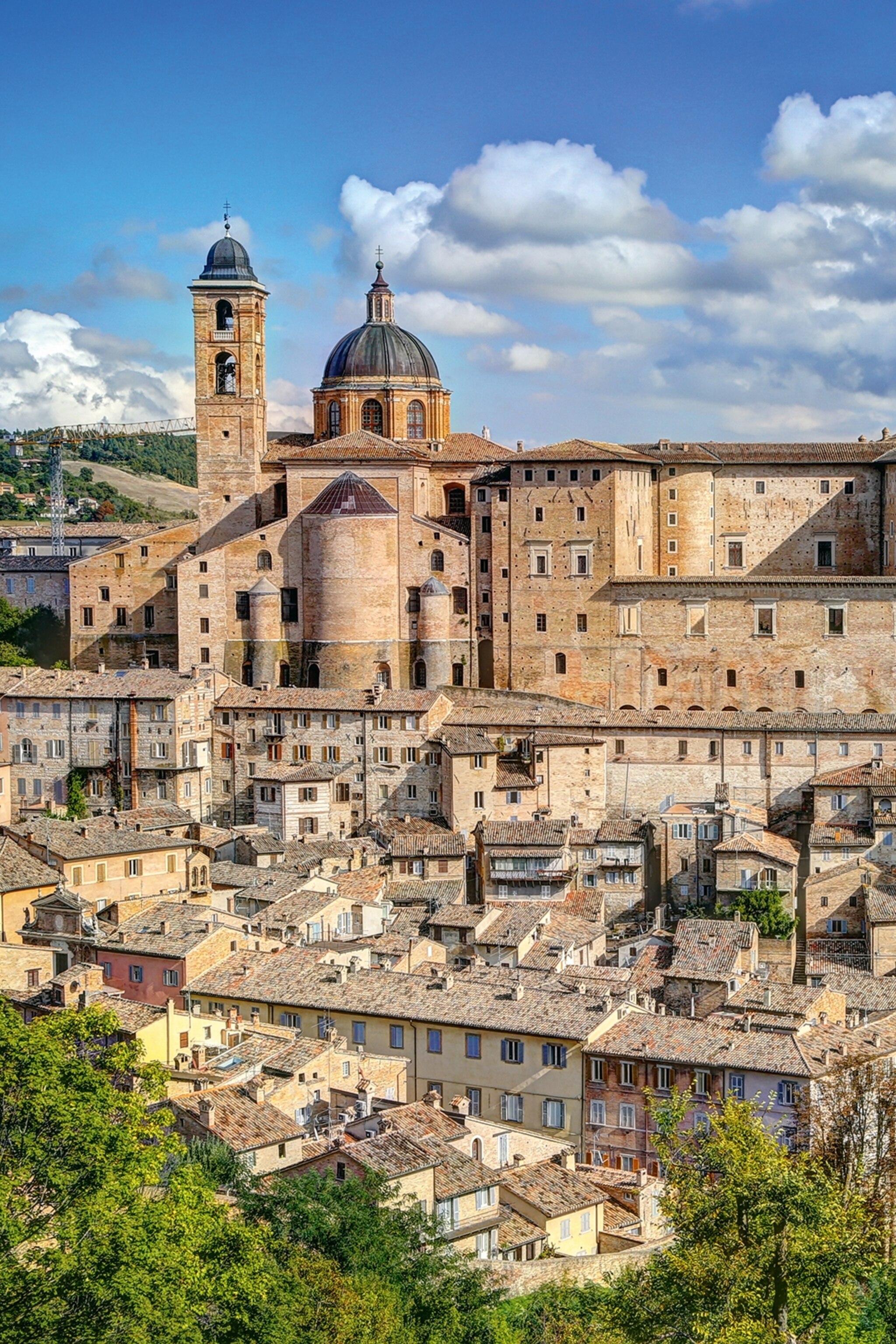 A medieval stone town set upon different levels in lush hills with a domed cathedral towering over the houses.