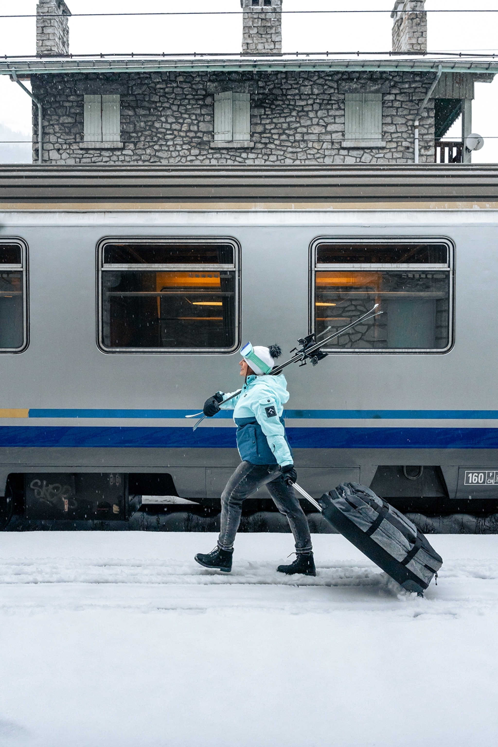 A female skier carrying her suitcase and ski past a train.