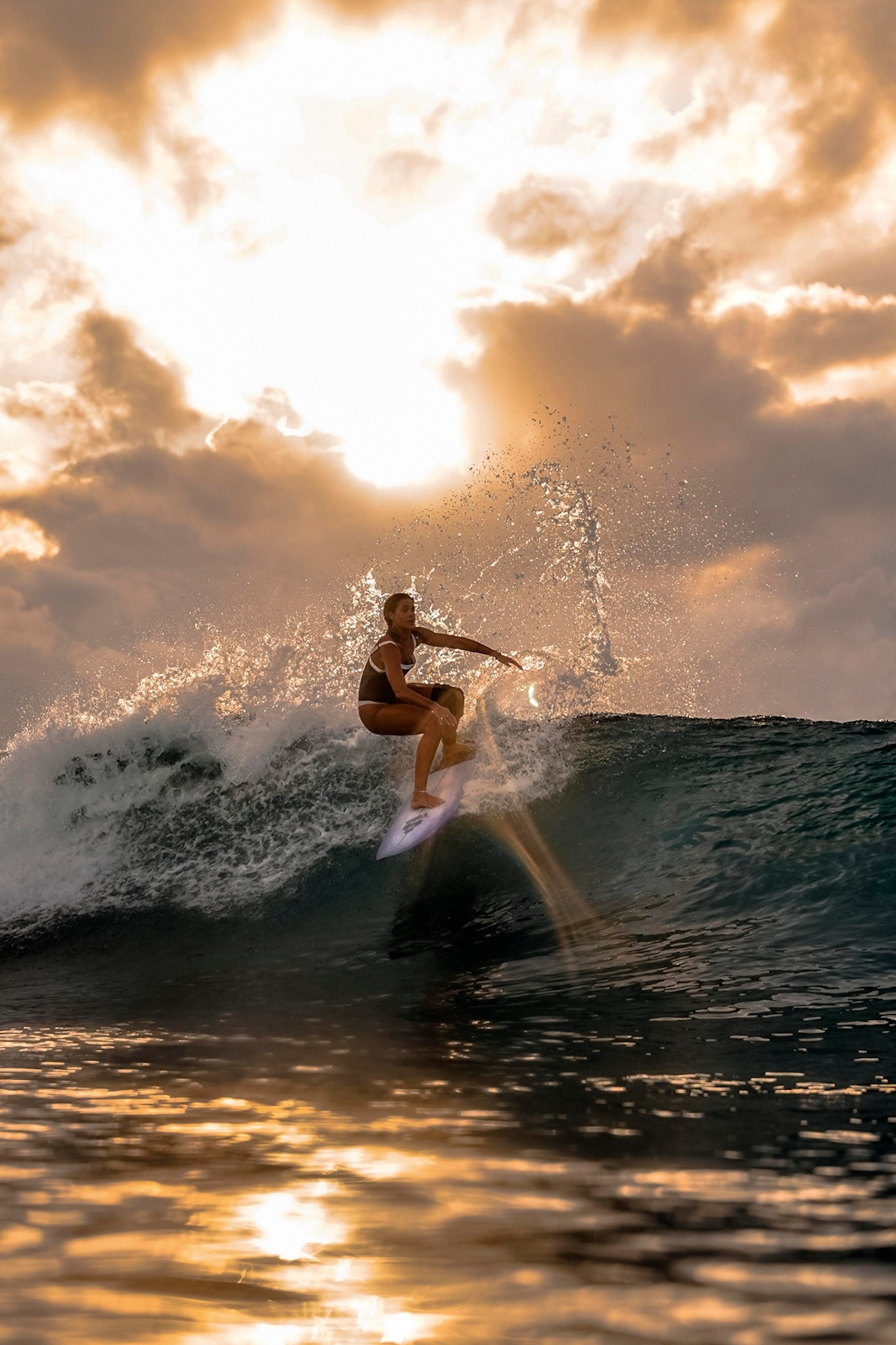 A dynamic ocean shot with a female surfer catching a wave at sunset.