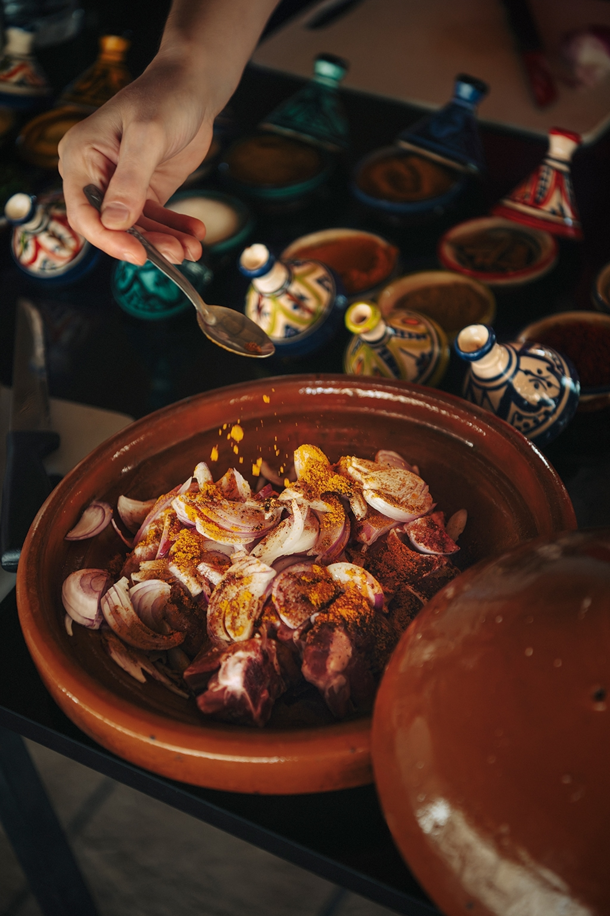 A close-up of the bottom half of a clay pot with diced red onion as someone is adding plenty of turmeric over the top.