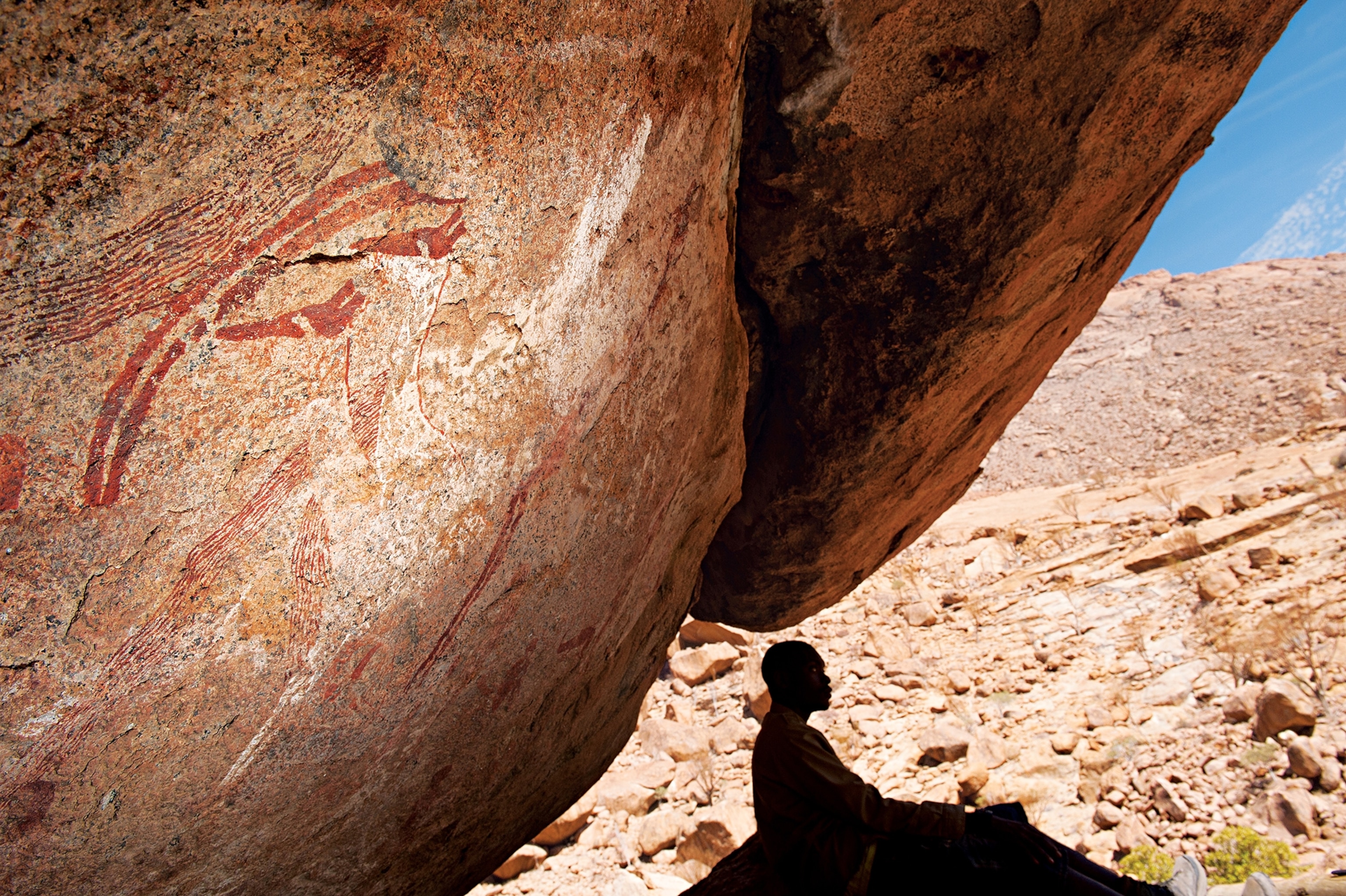 a Namibian guide sitting under a rock painting at the Tiara Shelter at Brandberg mountain