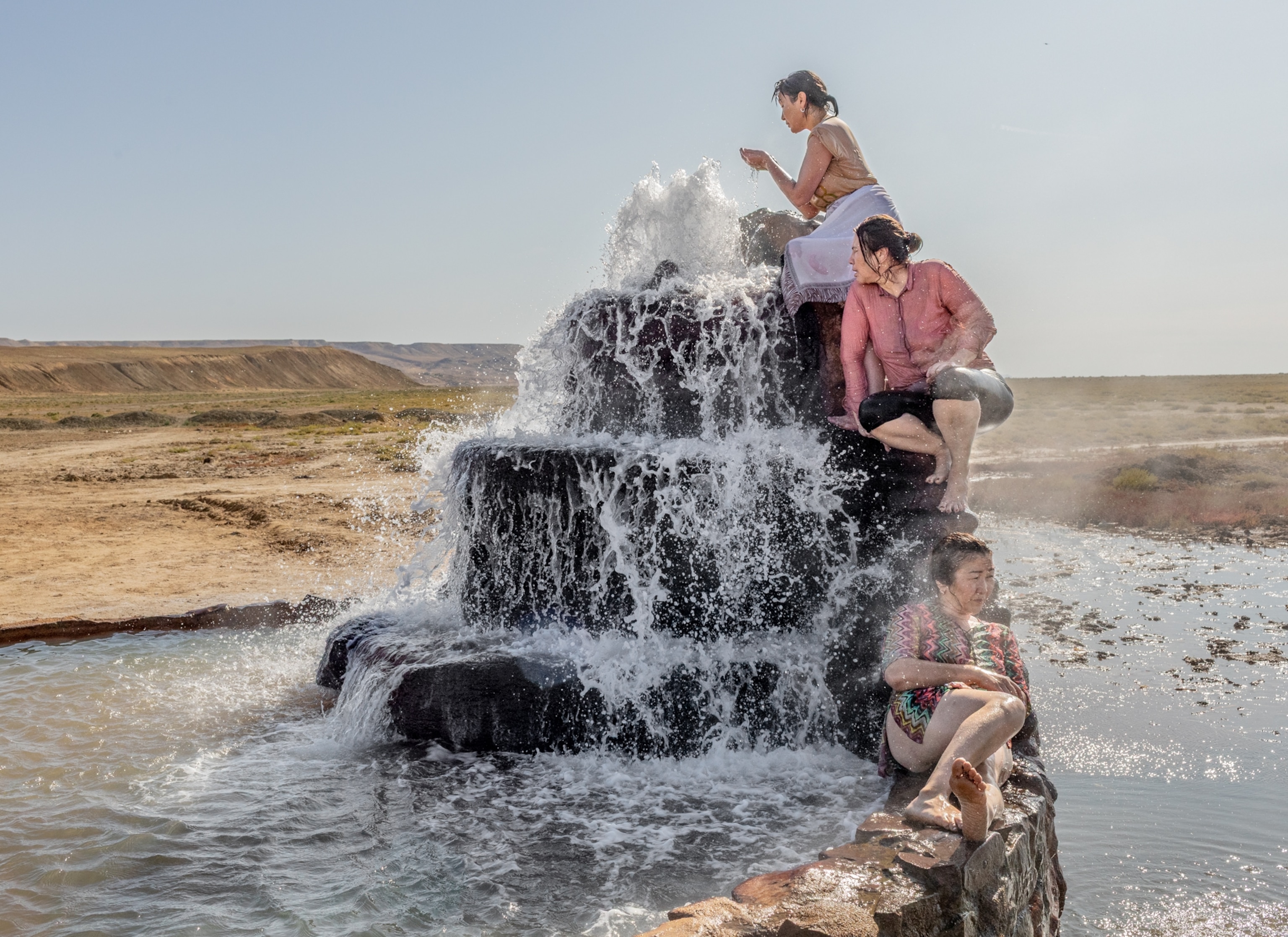 Water babbling and cascading from three tiers of rocks and three women sitting on each of them.