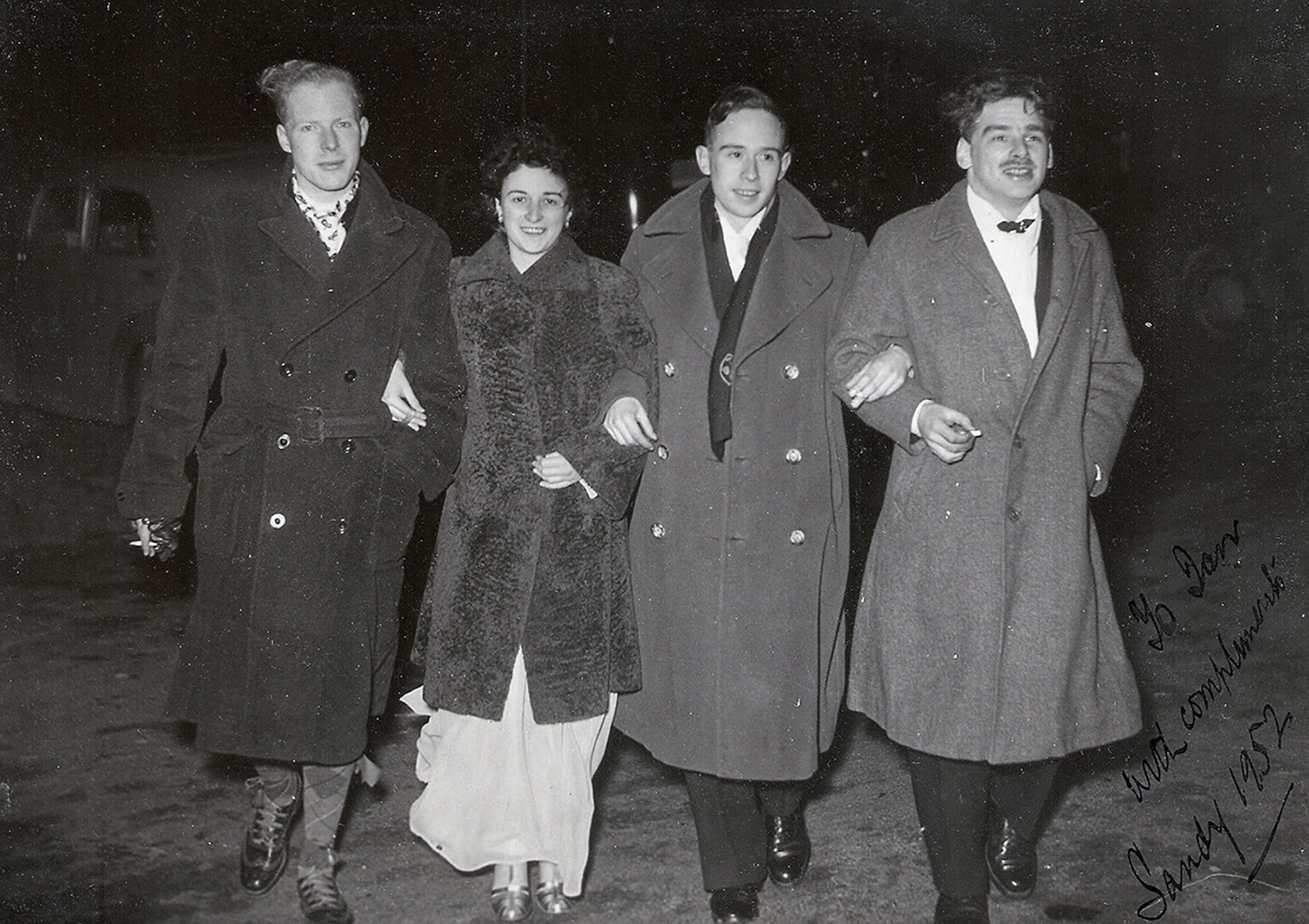 A group of four walk arm and arm toward the camera