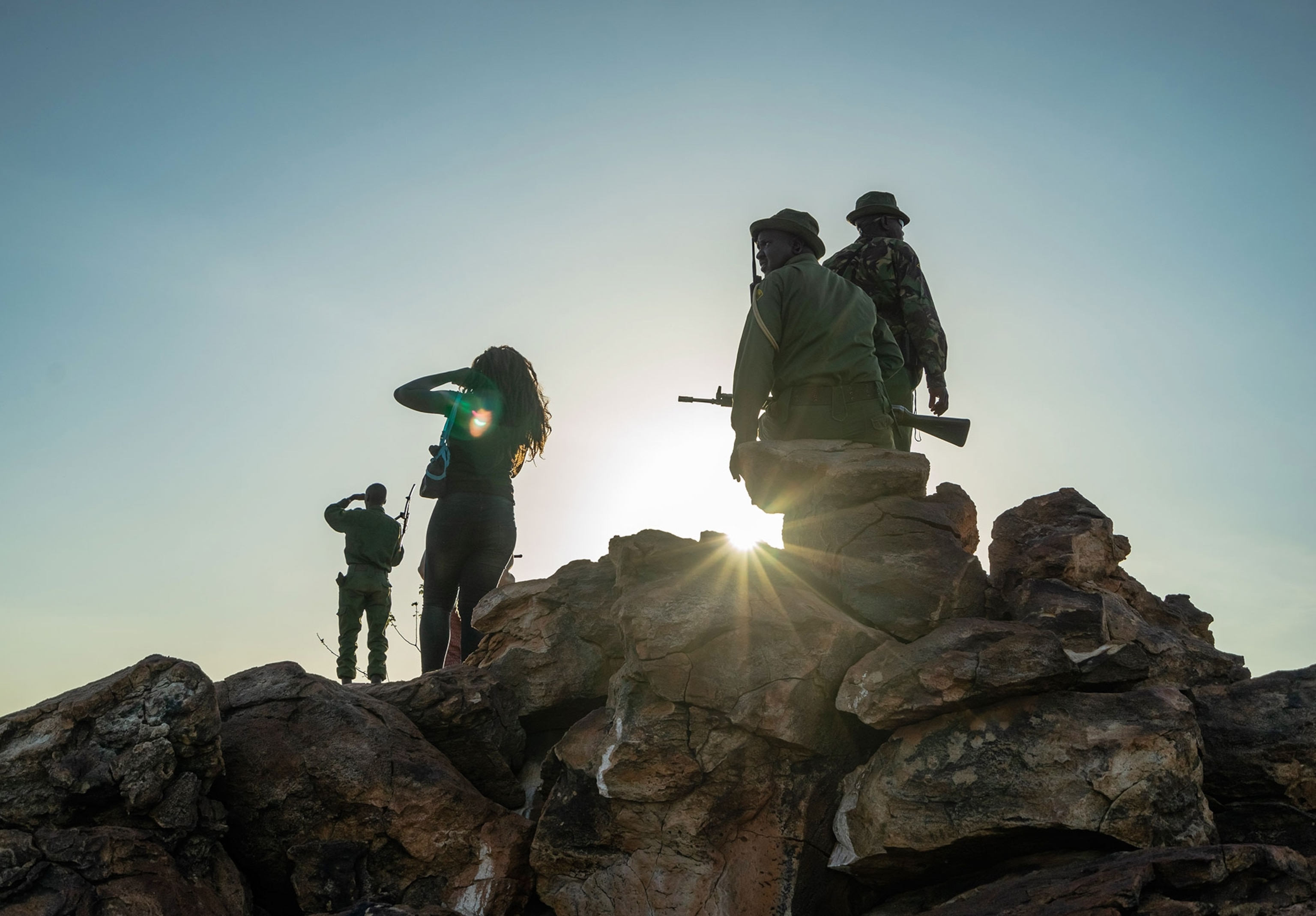 A group of people stand on a ledge shiloetted.