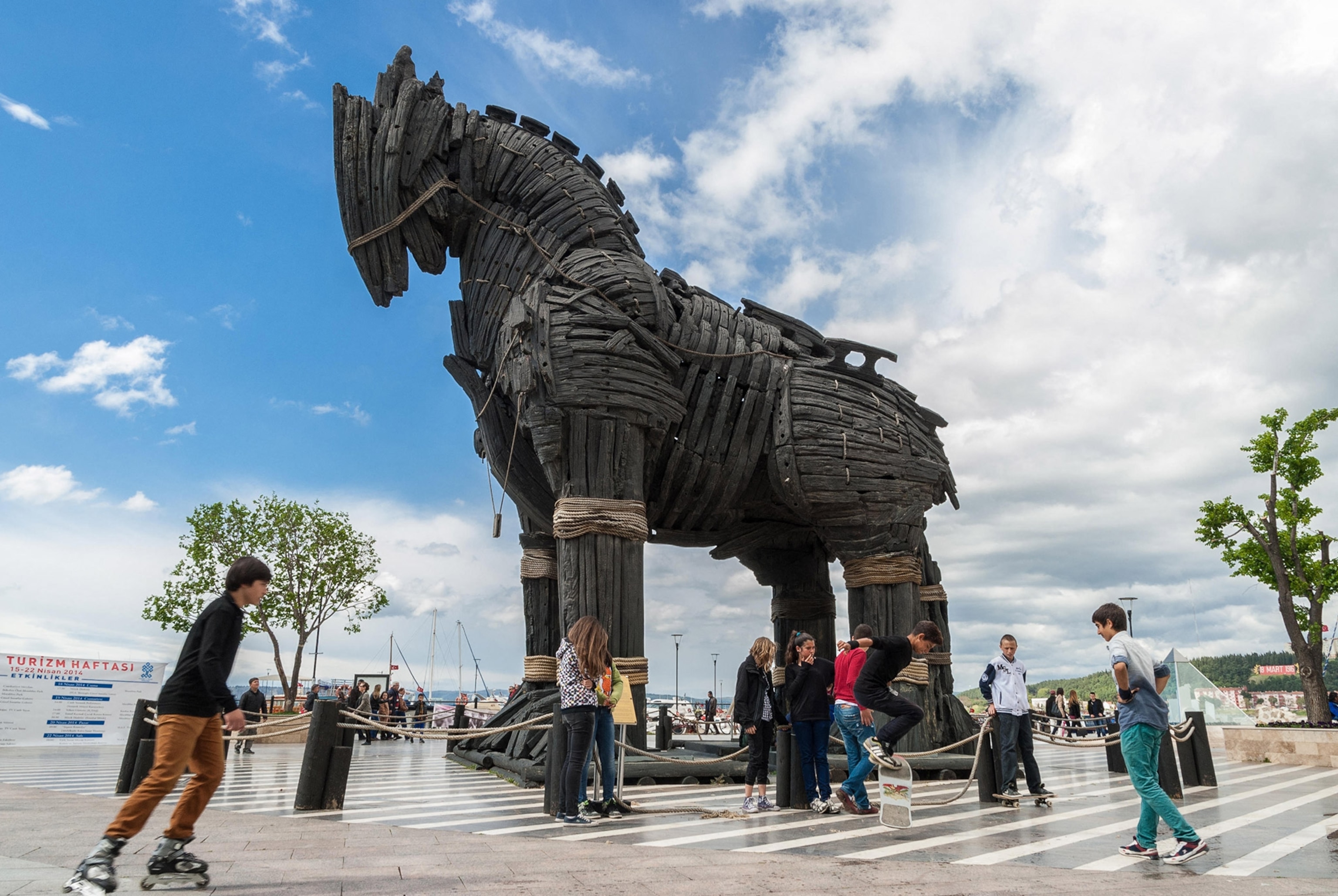 A large wooden horse statue in an open outdoor area with teenagers skating and standing around