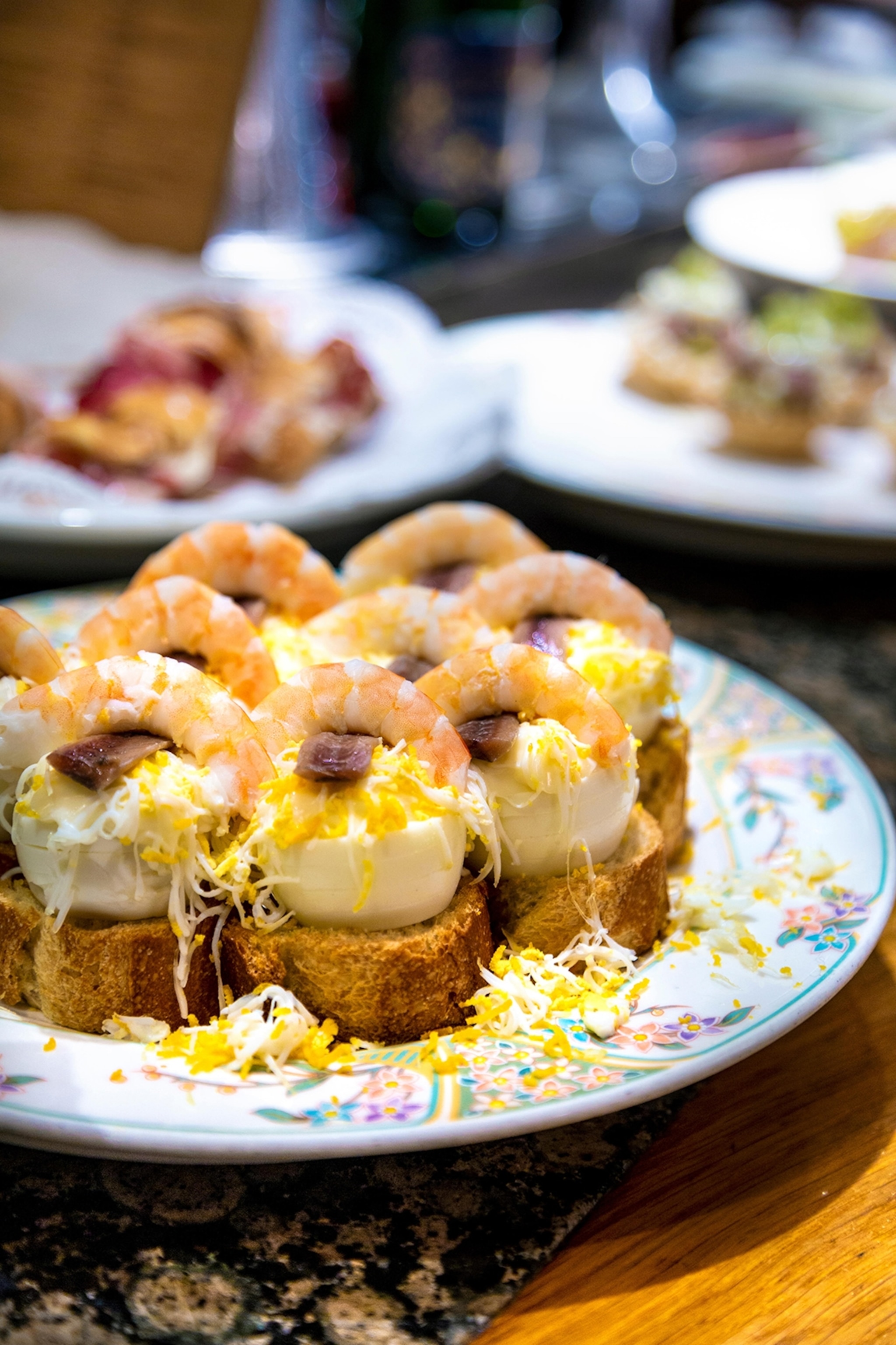 A plate of eight small tarts topped with cheese and shrimp.