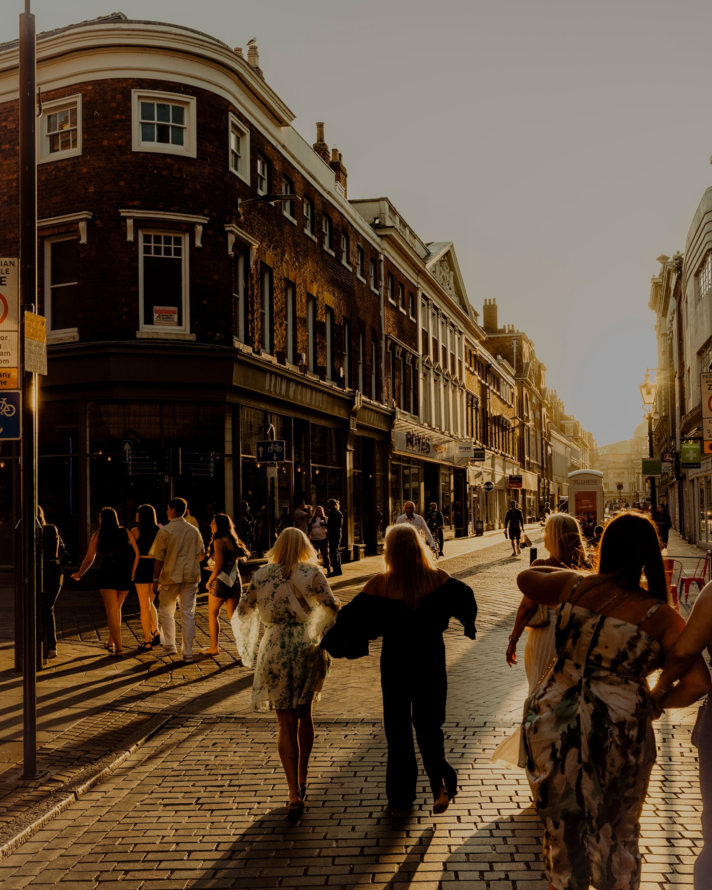 Hull, United Kingdom — July 2025: Scenes from Hull’s maritime heritage and community, showing a view down Whitefriargate with Saturday night revelers in the street as the sun sets behind them.