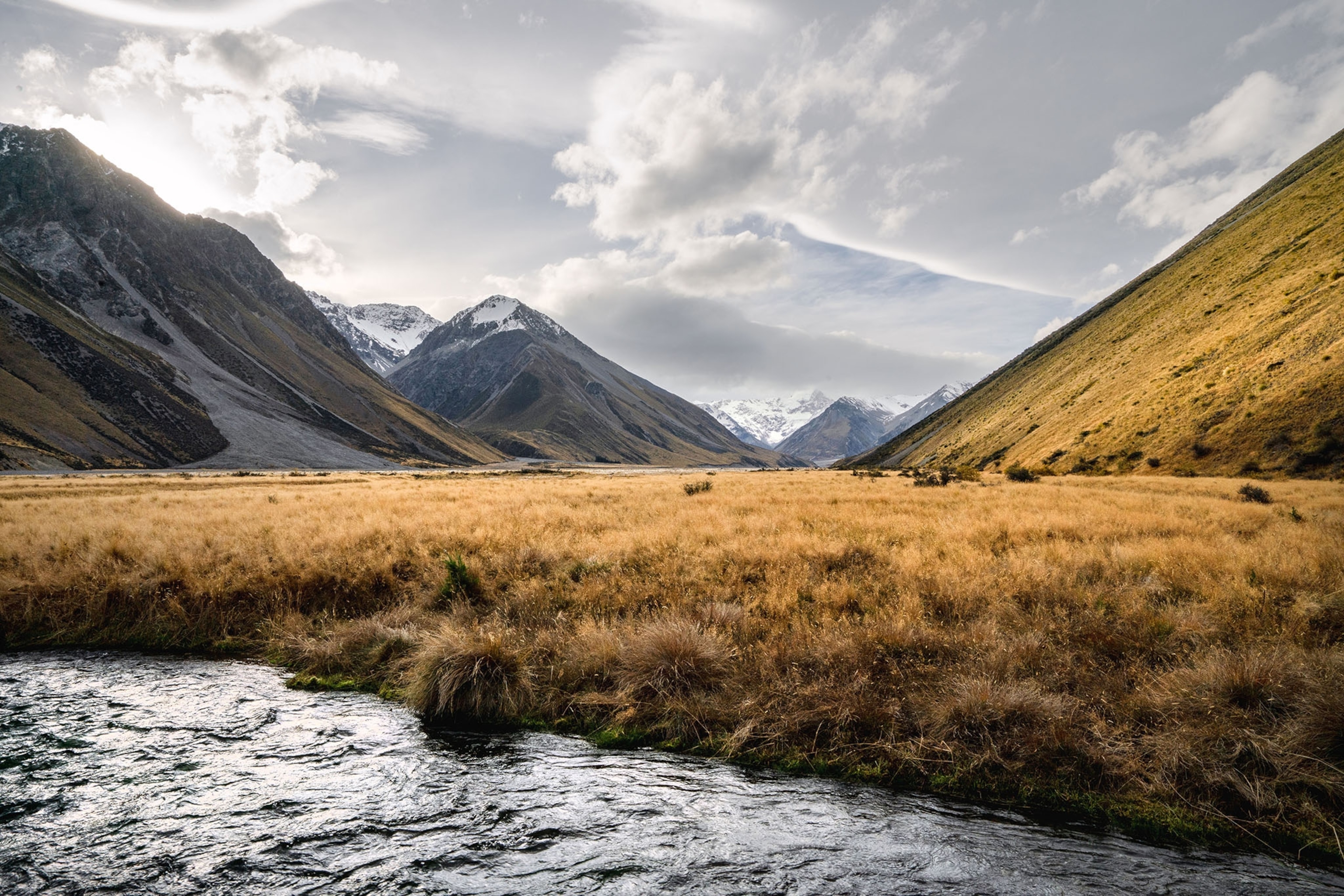 A windy landscape with a river coursing along the foreground and mountains in the background.