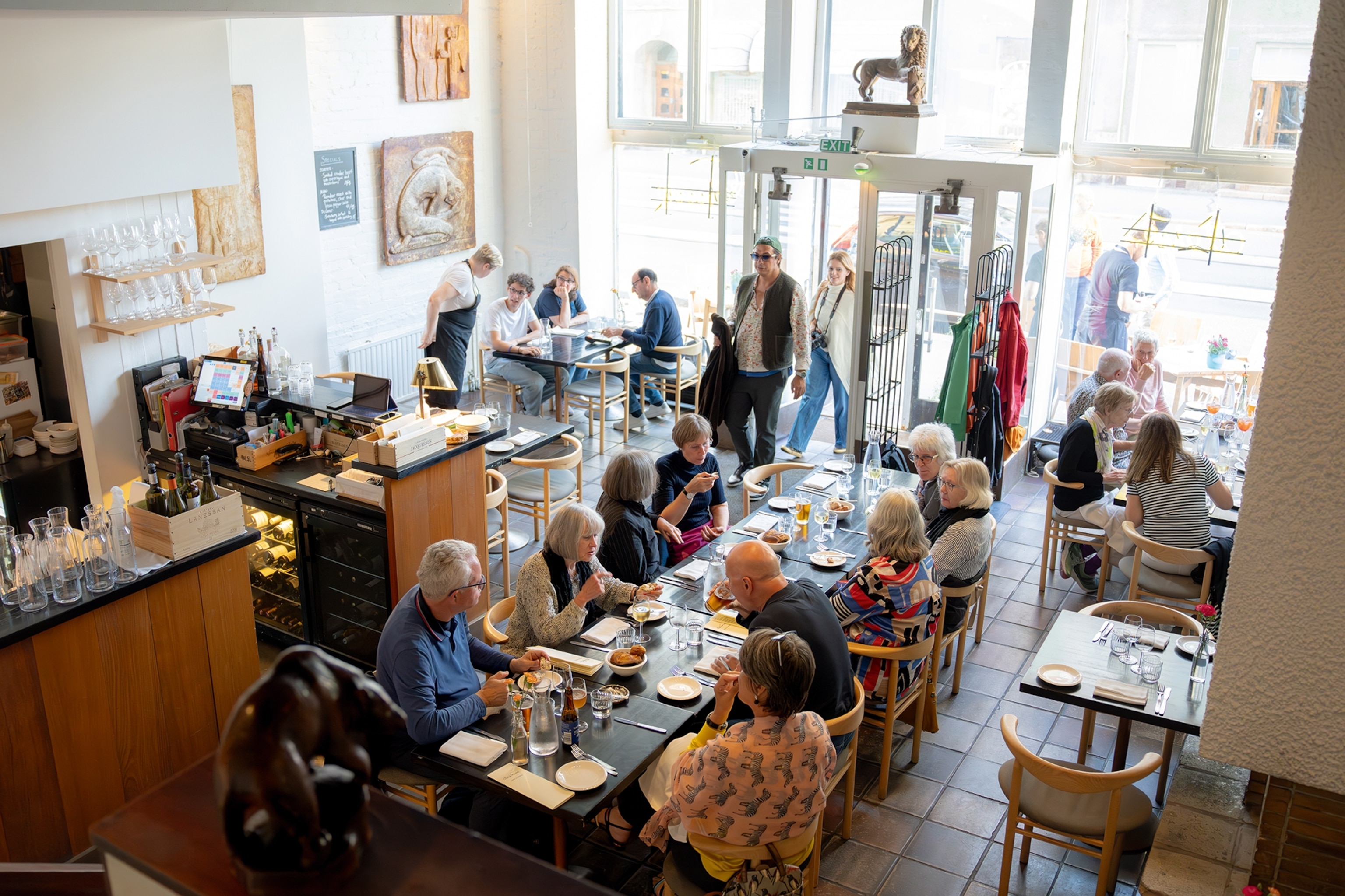 A busy, open-plan cafe with a bright window front and a long, communal table in the centre.
