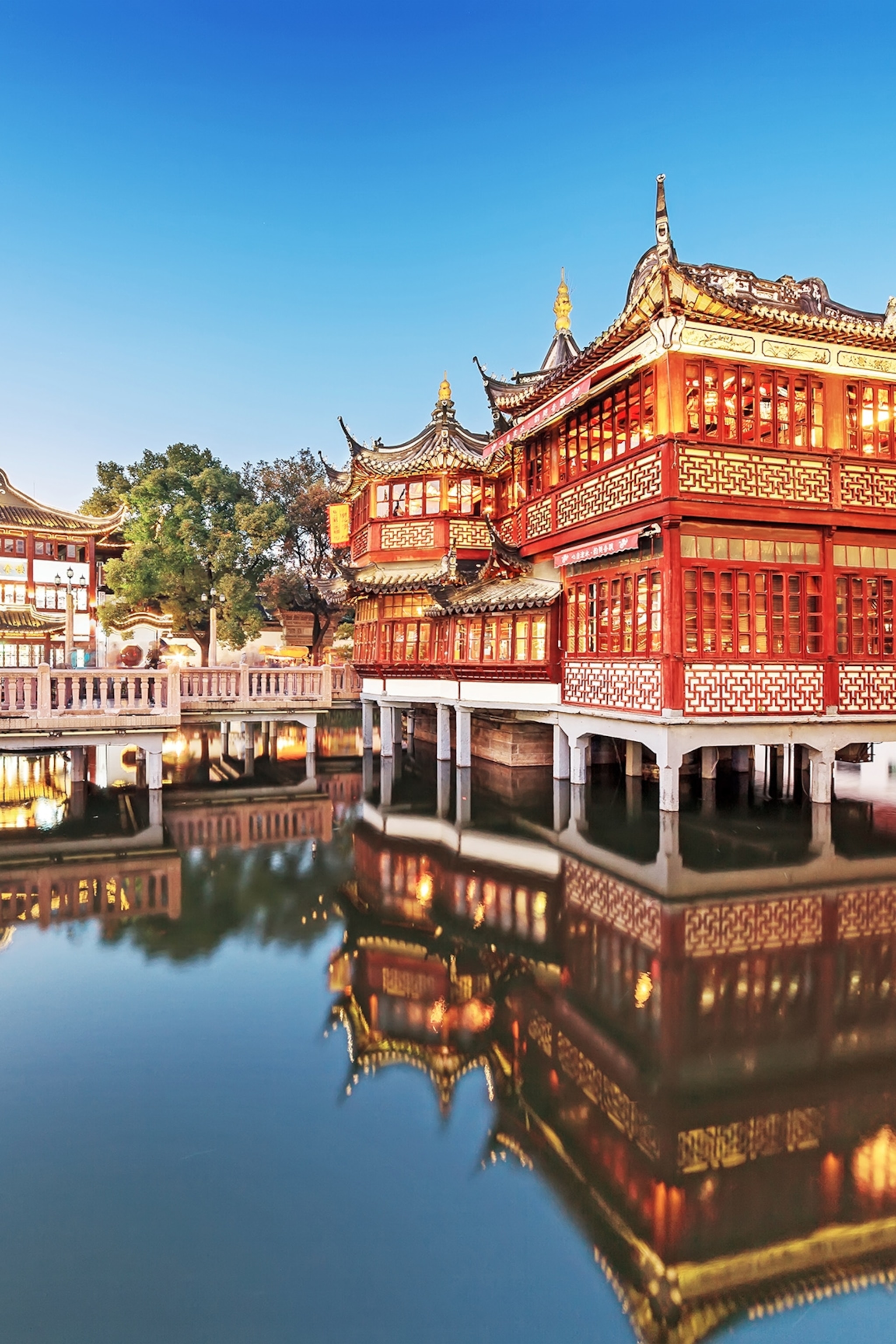 A set of temples with lanterns build on a lake with trees in the background.