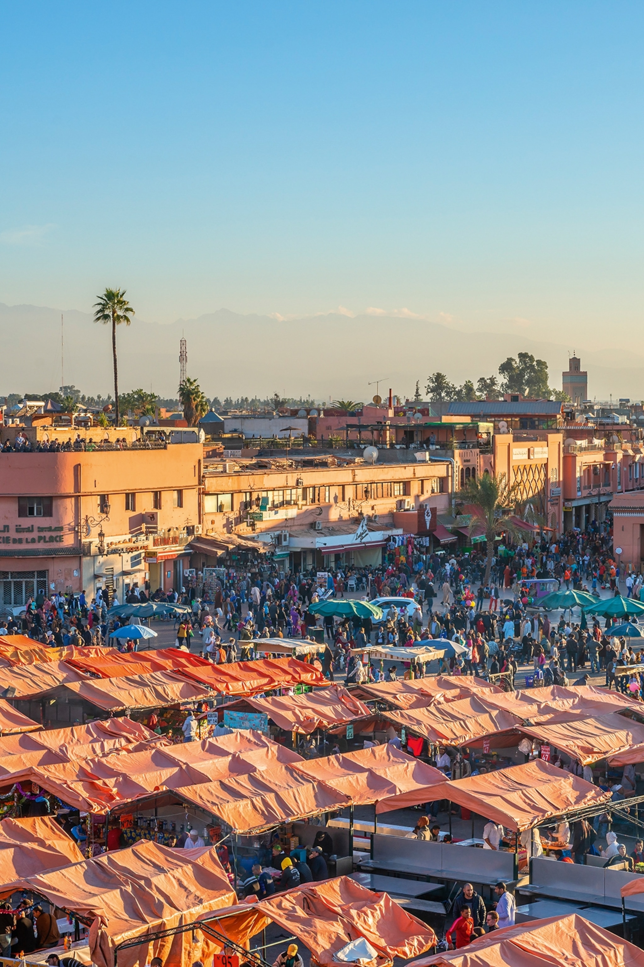 An aerial view over a busy medina market in Morocco with shaded stalls on a plaza.