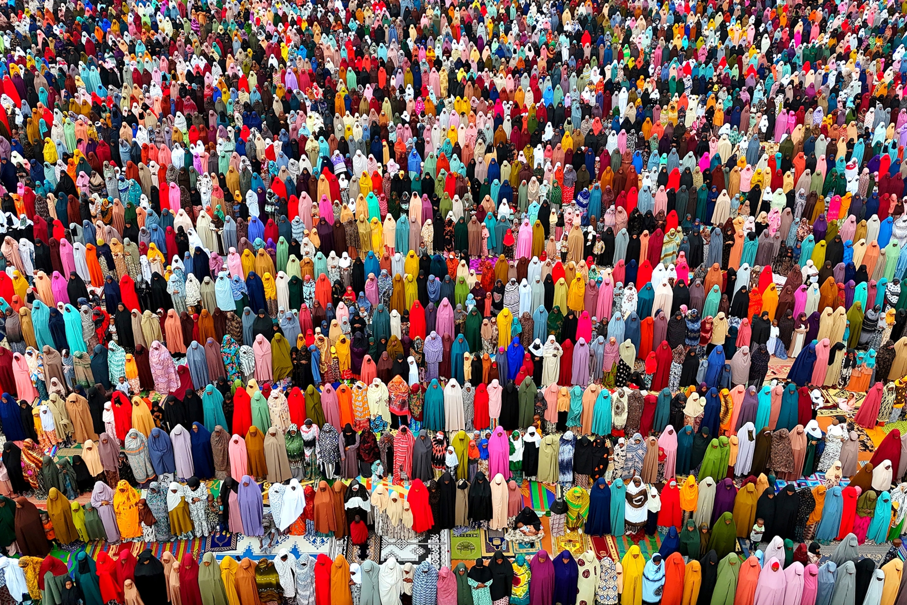 A sea of clothed people with prayer rugs in front of them.