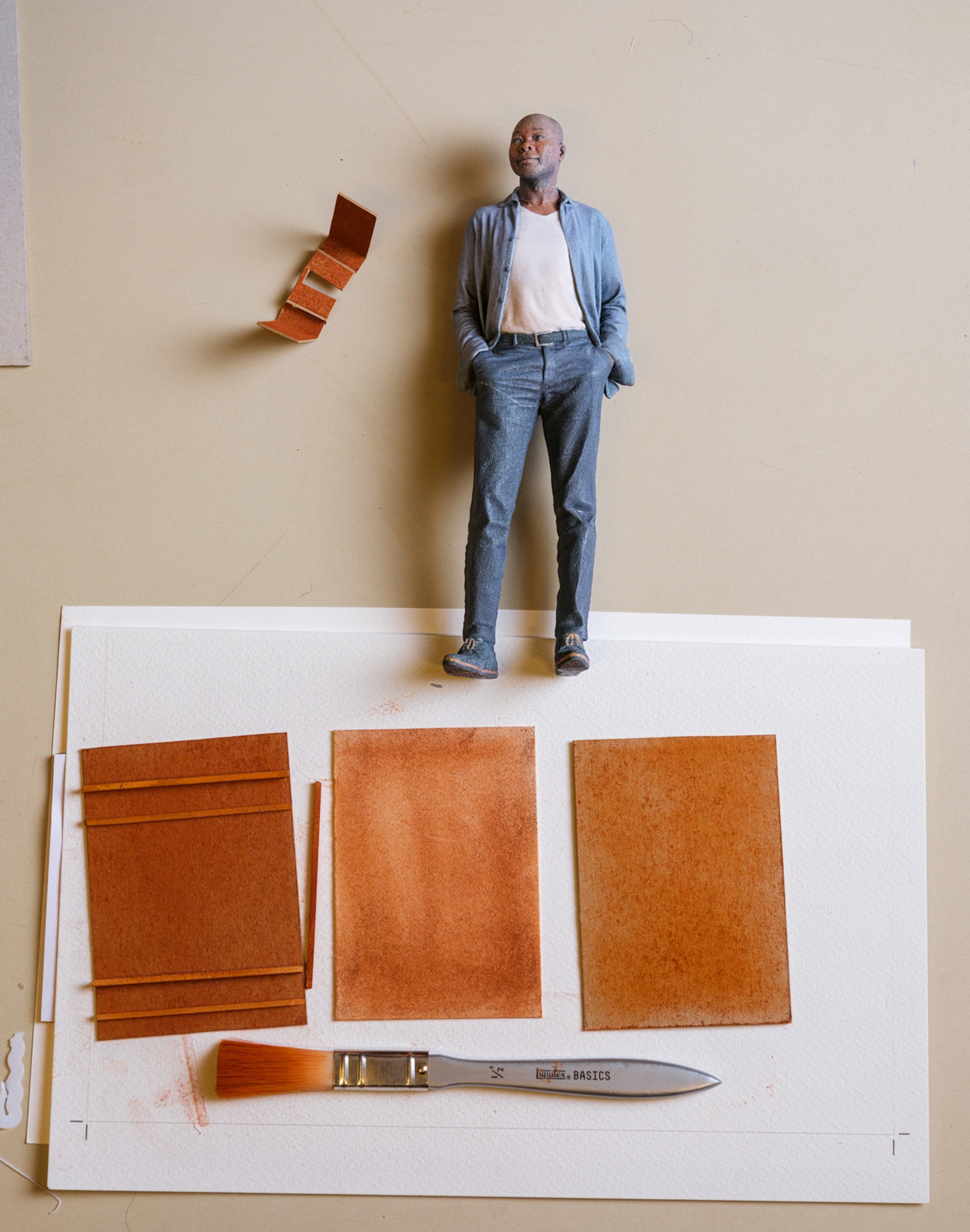 A little figurine of a man lays on a table with a paintbrush and swatches of orange