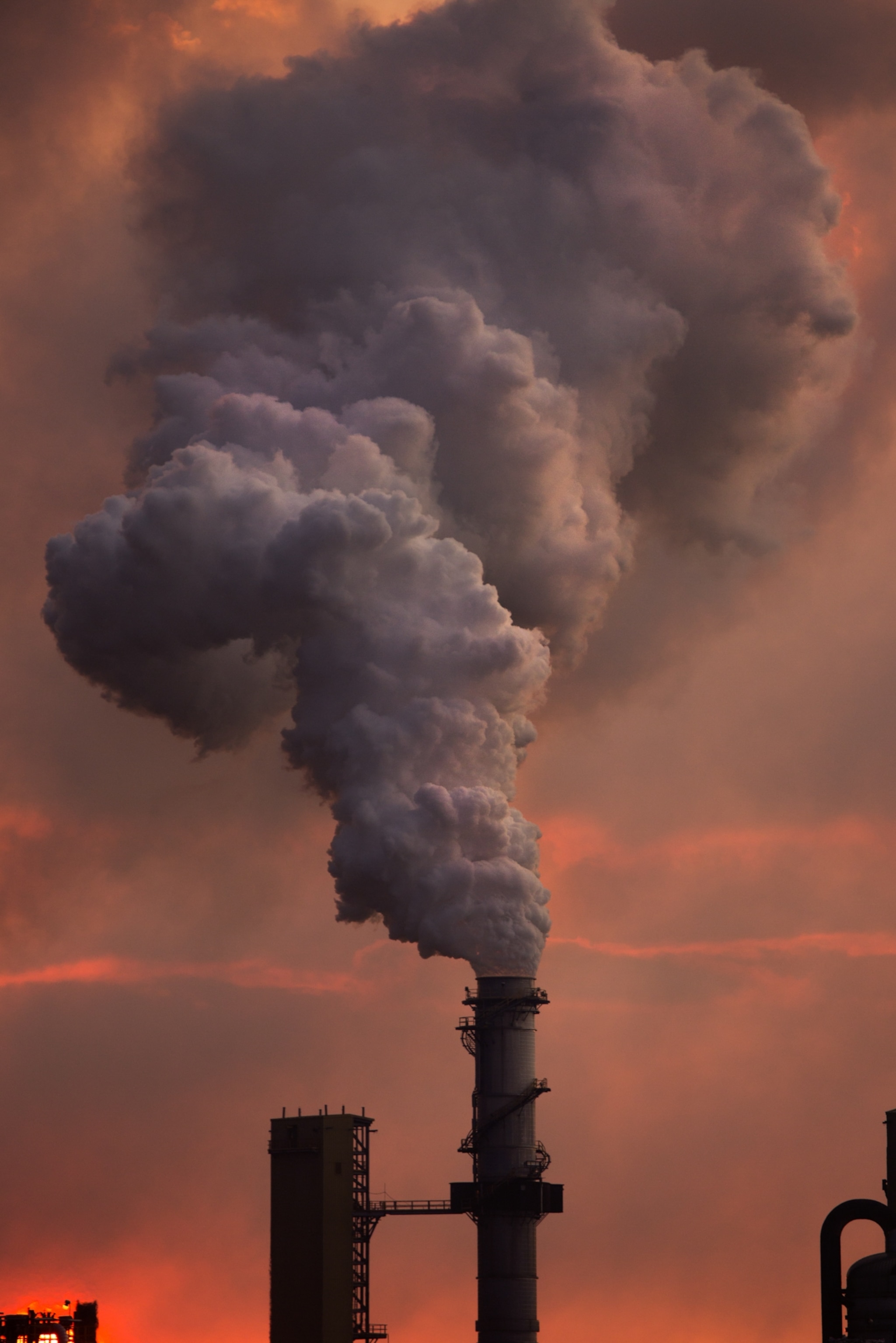 Smoke pouring from a smokestack against the backdrop of a cloudy, red sky