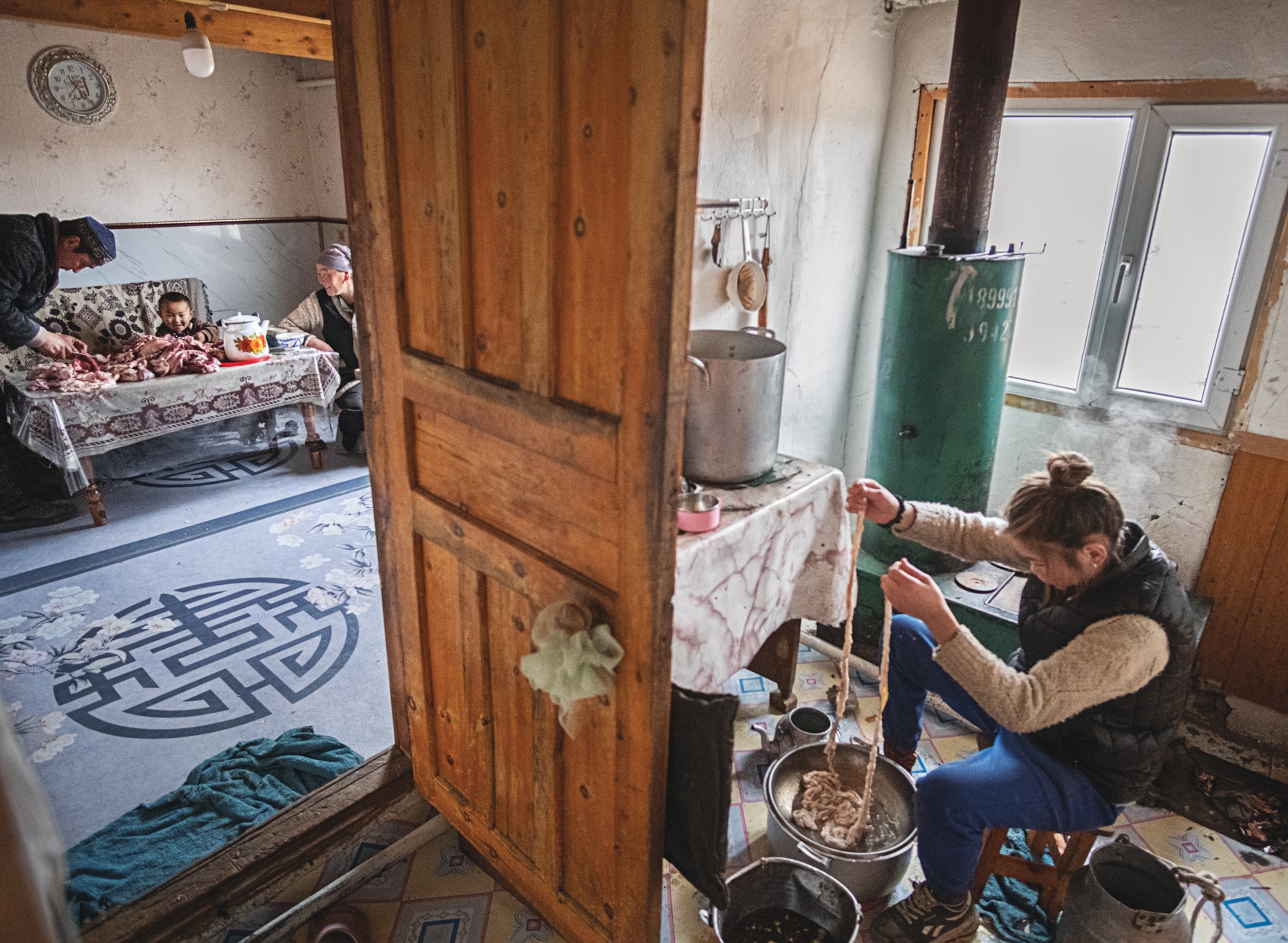 Woman working in the kitchen while family members cutting meat in the nest room seeing through open door.