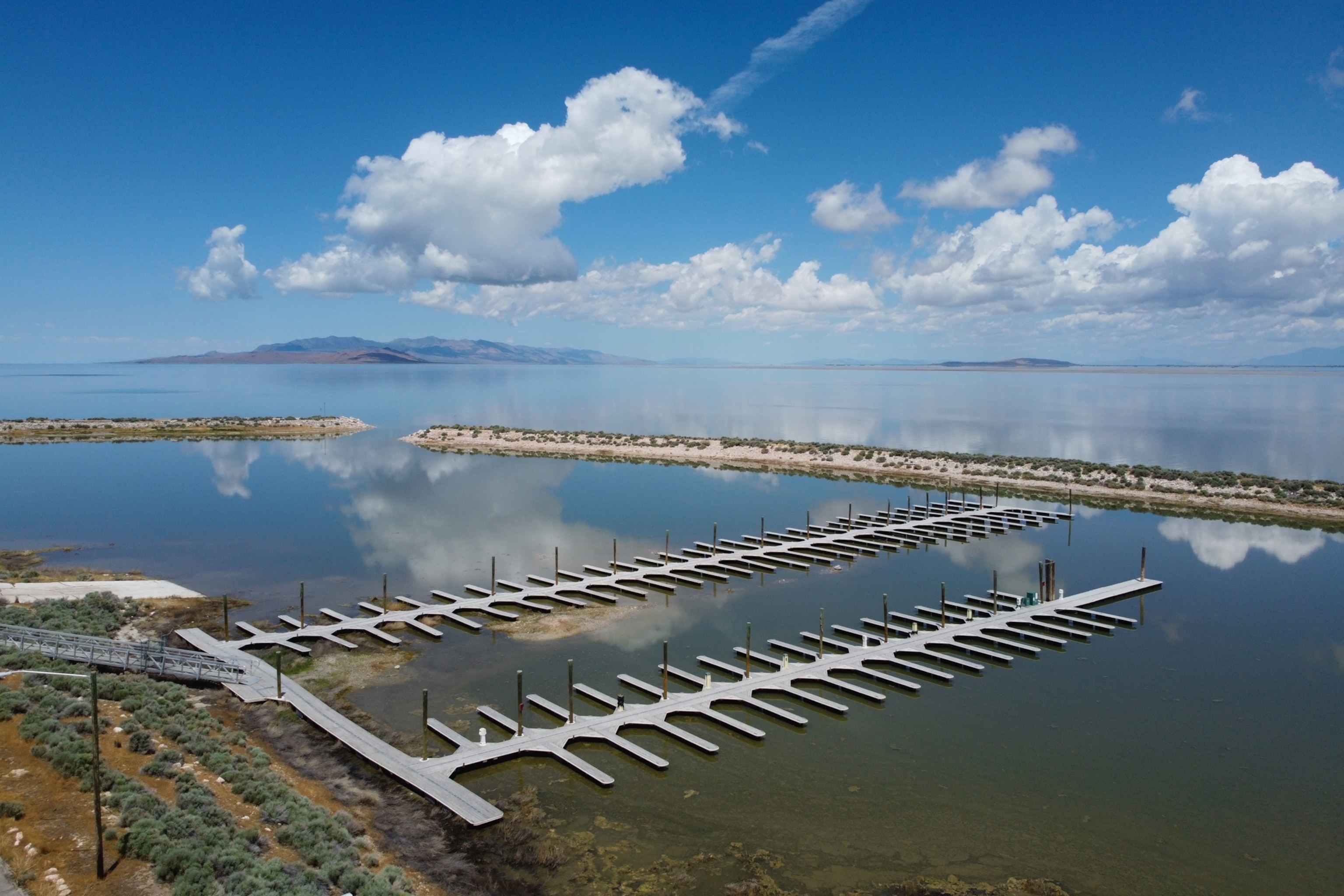 Aerial view of an empty marina on a calm, reflective lake with a mountain range in the background.