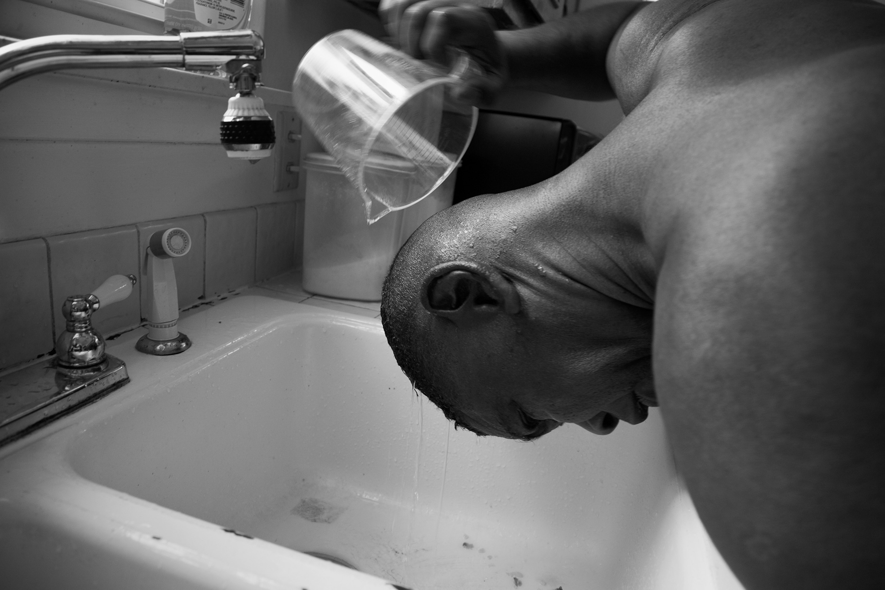 man rinsing head under faucet