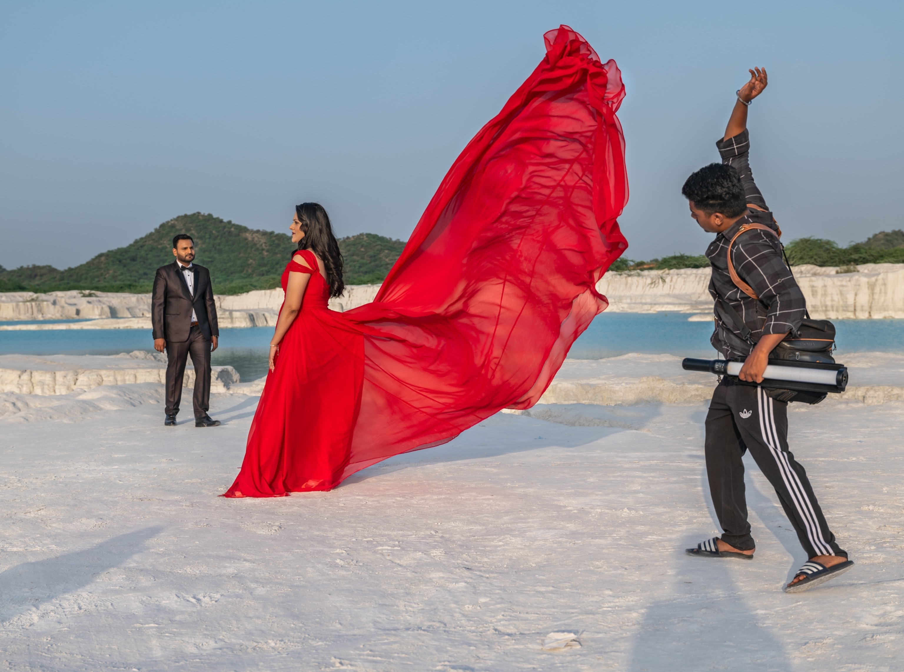 A man in a suit stands in front of a woman in a red flowy dress that a photographer cascades in the air.