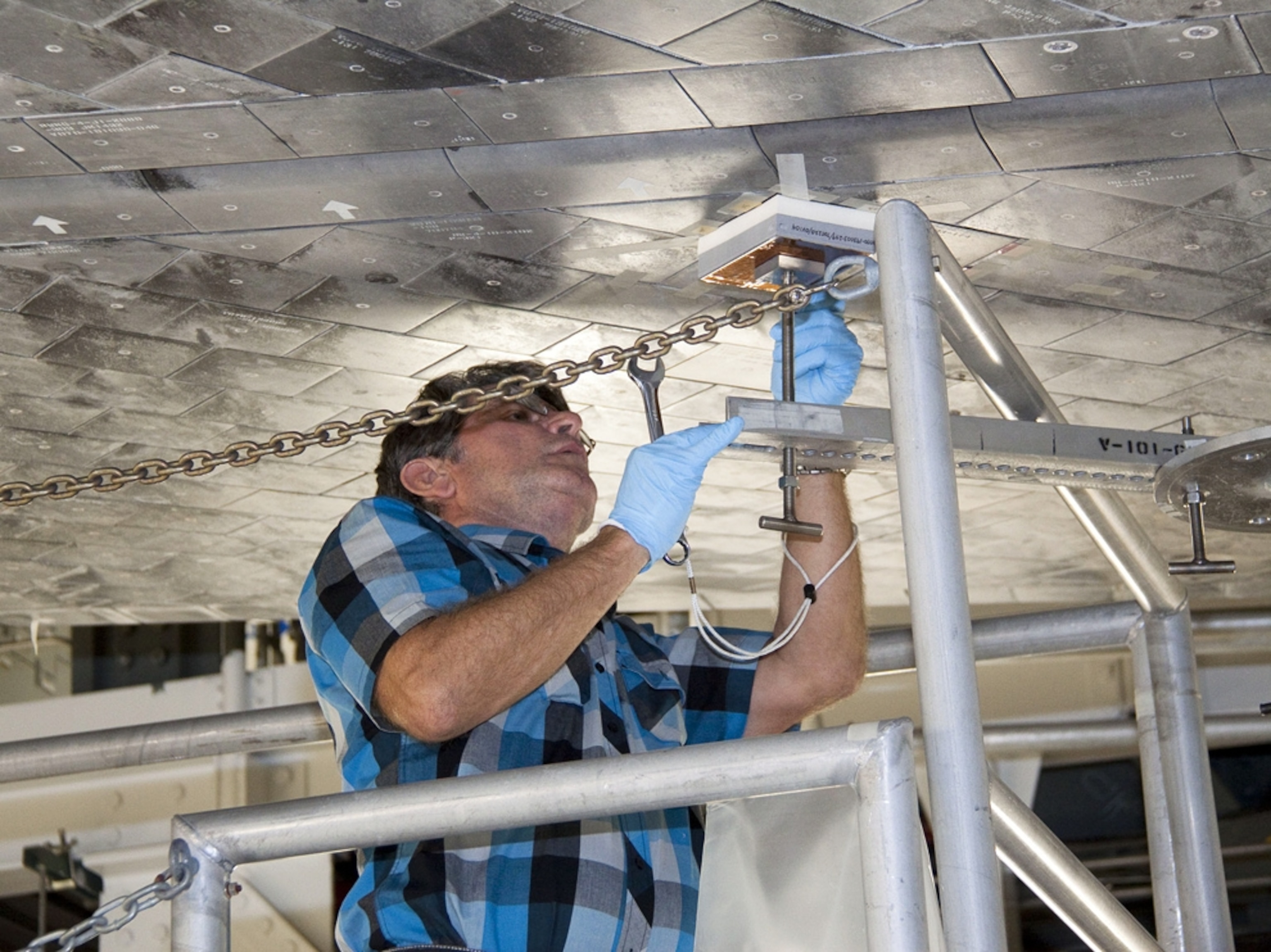 a worker attaching a heat-shield tile to the underside of the space shuttle Atlantis