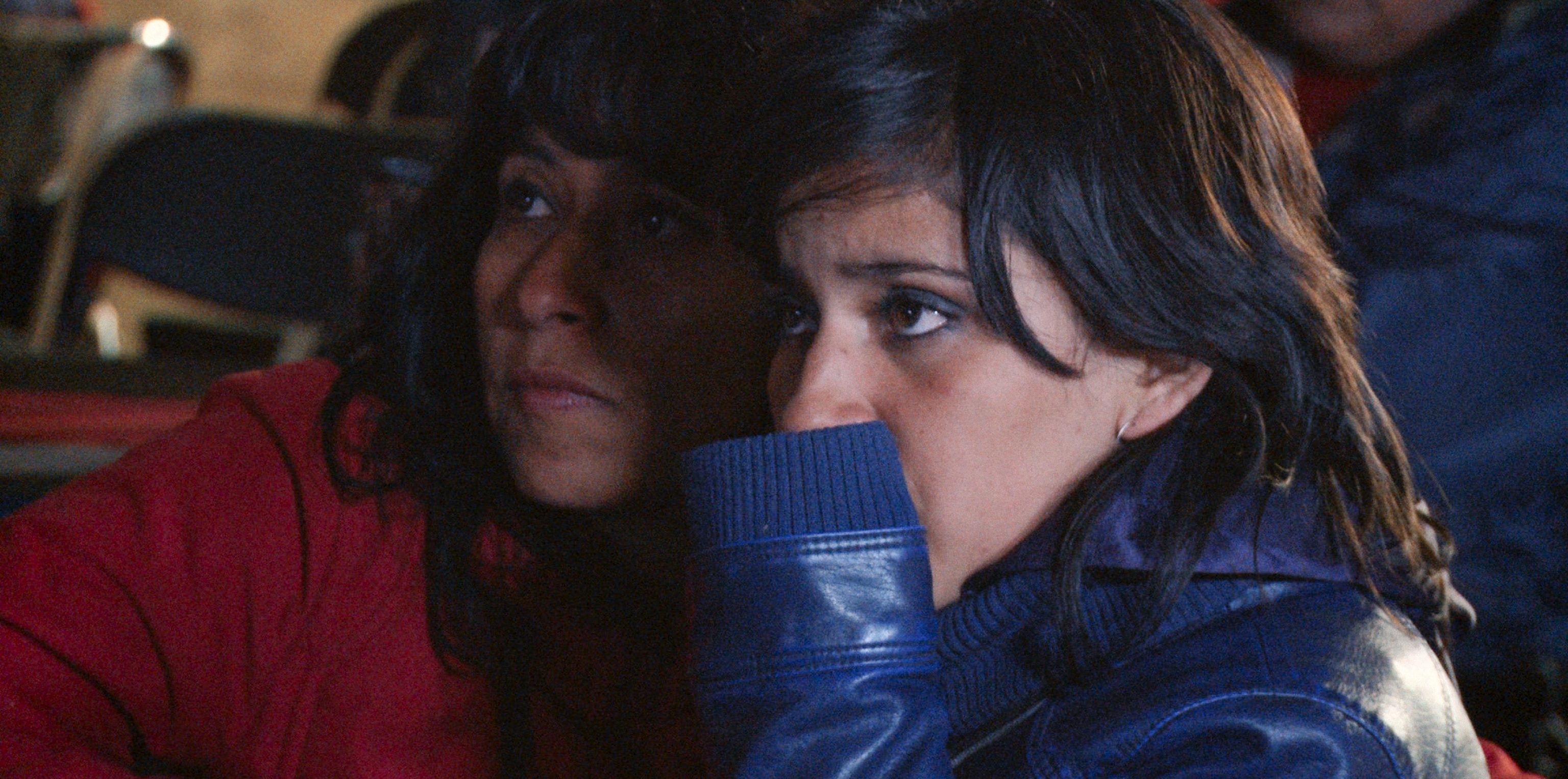 Two women hold each other close with anxious expressions on their faces.