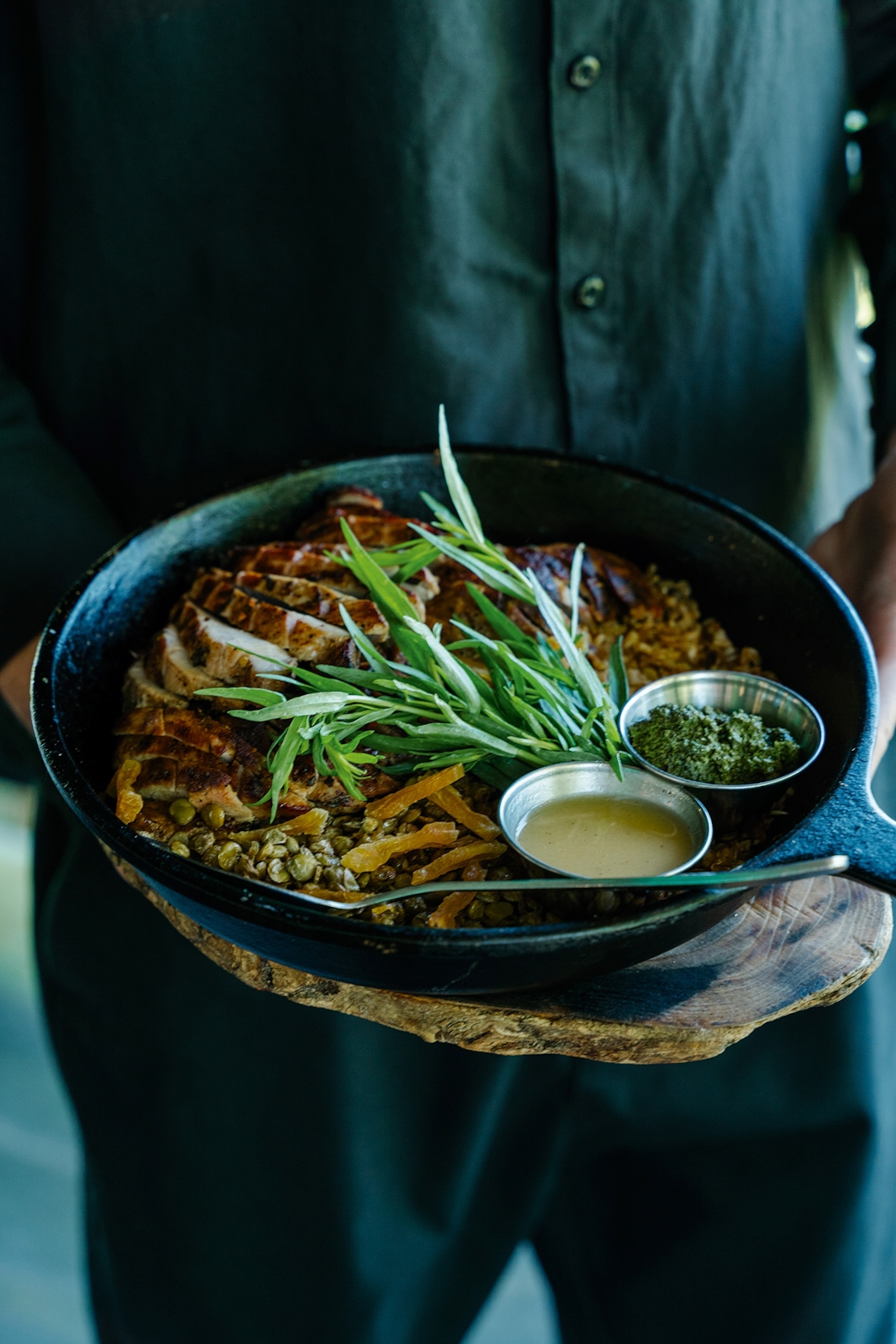 Sliced and roasted turkey breast served alongside grains and two sauces in a cast iron pan.