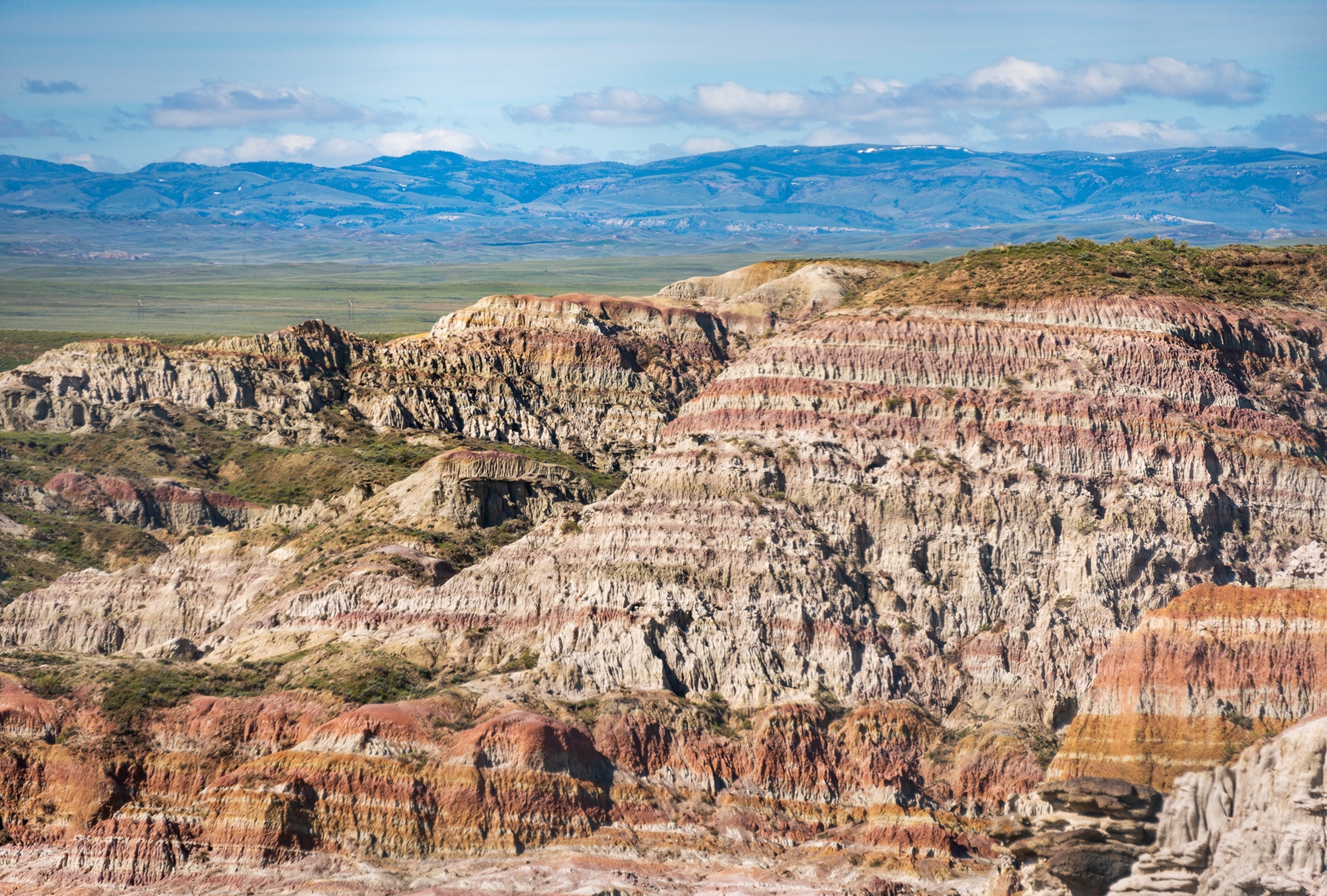 A sprawling landscape with colorful rock formations in front of blue mountains.