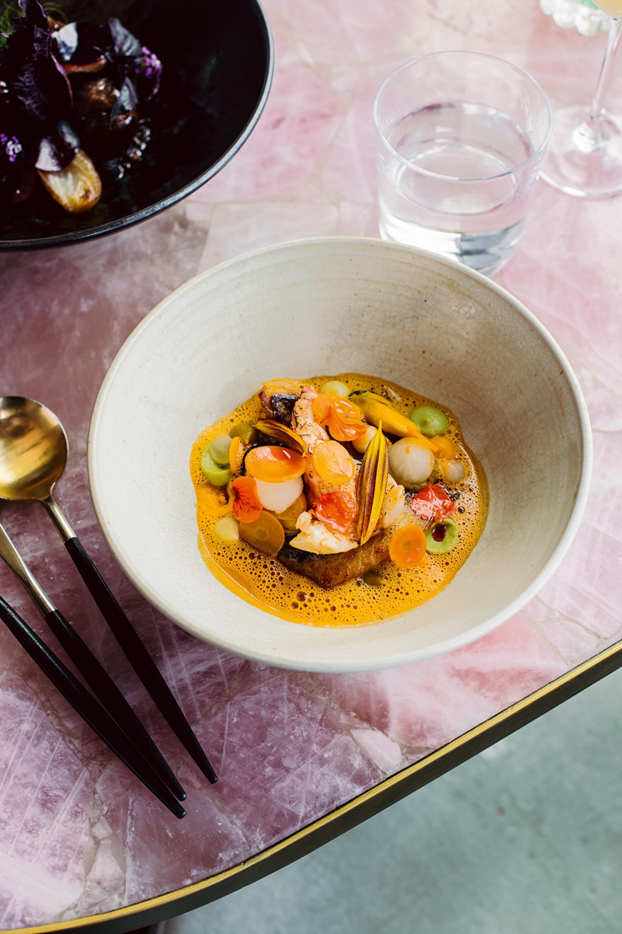A close-up of a fine-dining dish with a spiced sauce under a pile of sliced carrots and more.