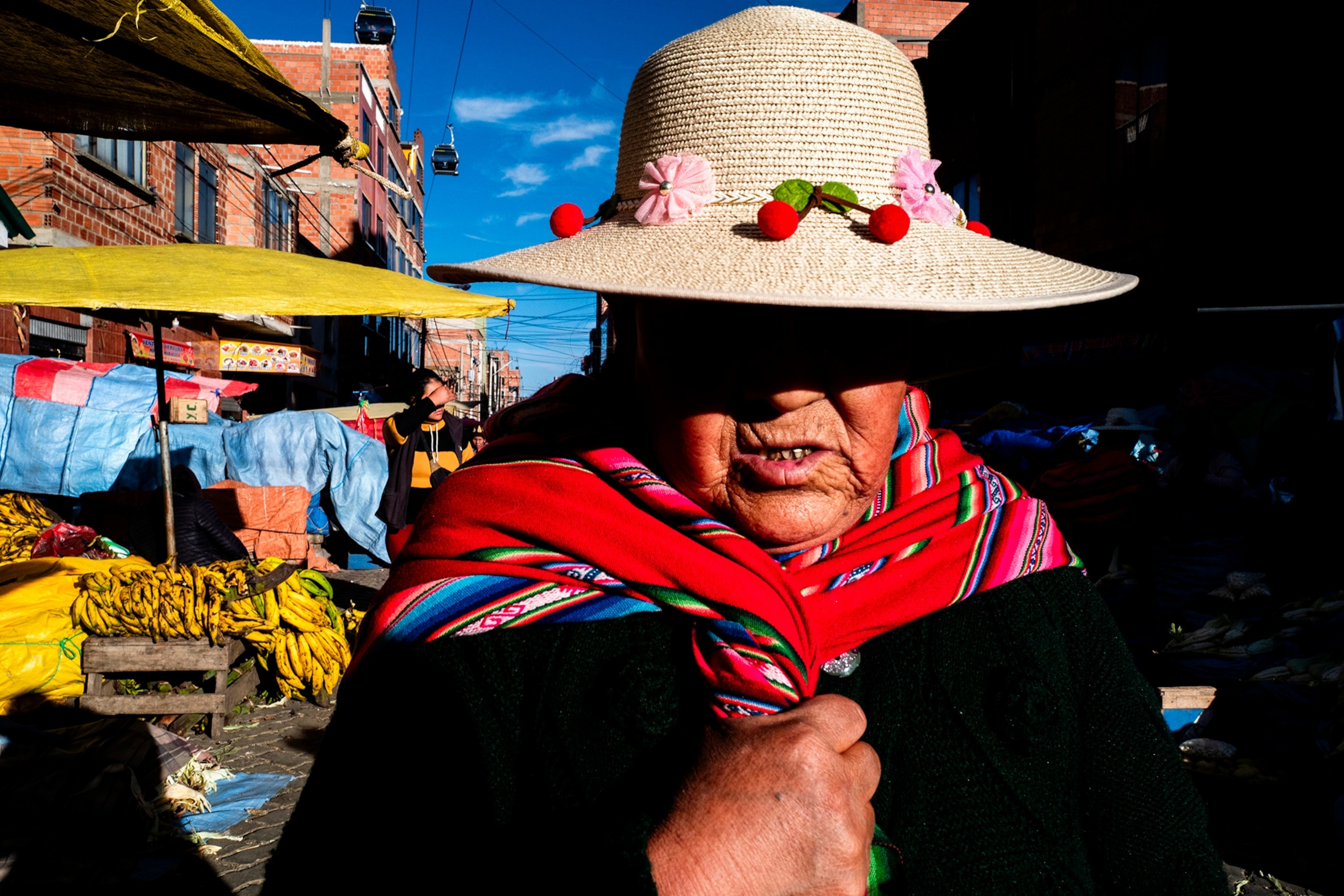 A person walks through a market wearing a beige hat and colorful clothing.