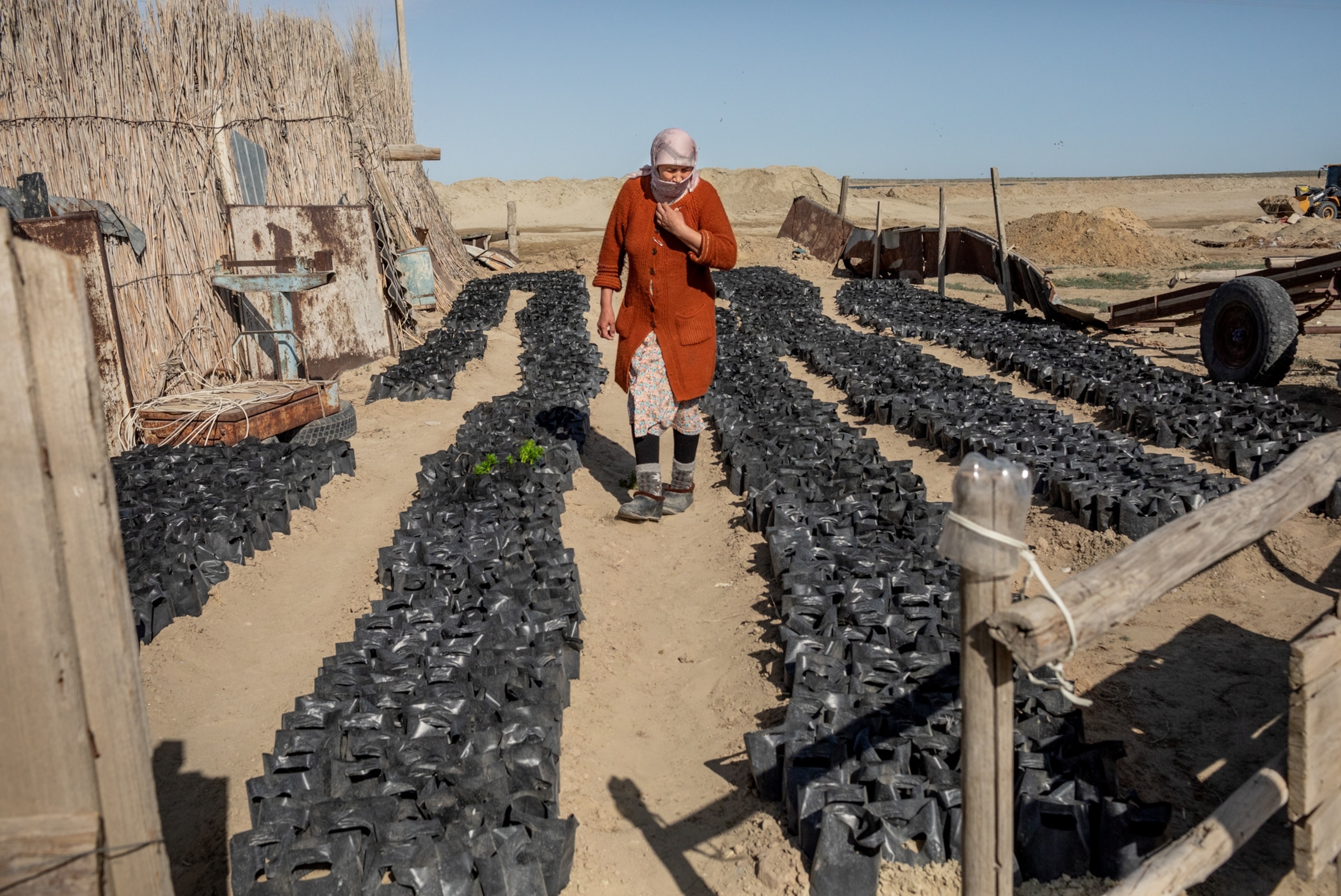 Woman in red coat walking along rows of black plastic bags.