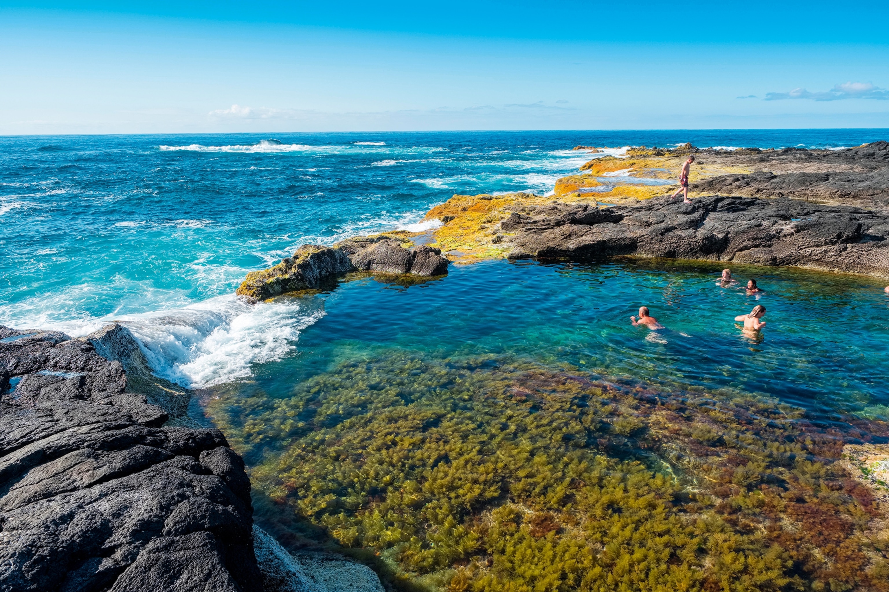 A wide shot of a natural pool leading into the ocean on one side.
