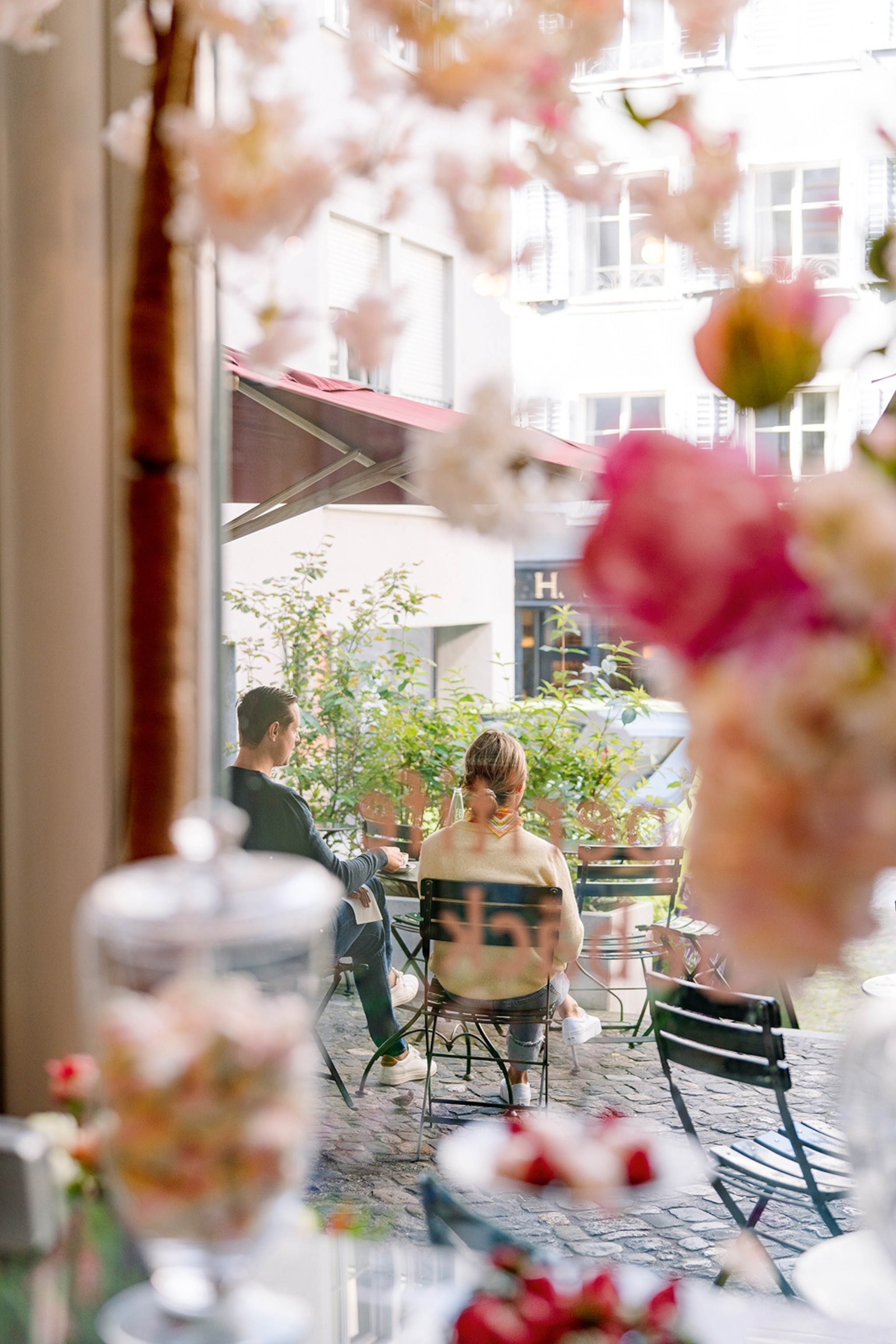 A voyeuristic shot through the window of a patisserie onto a couple sitting on the patio outside.