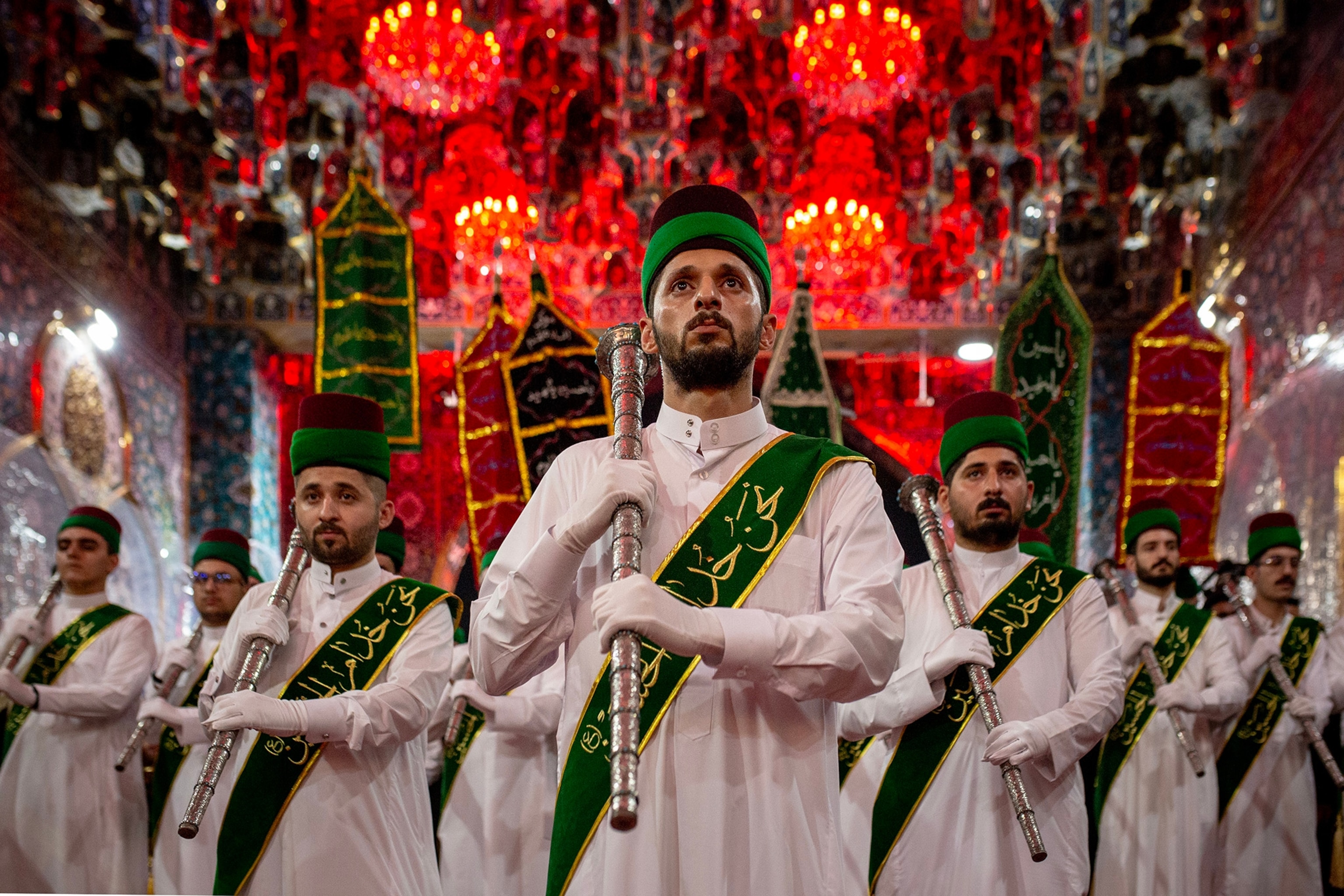Men wearing white shirts and green sashes march in procession