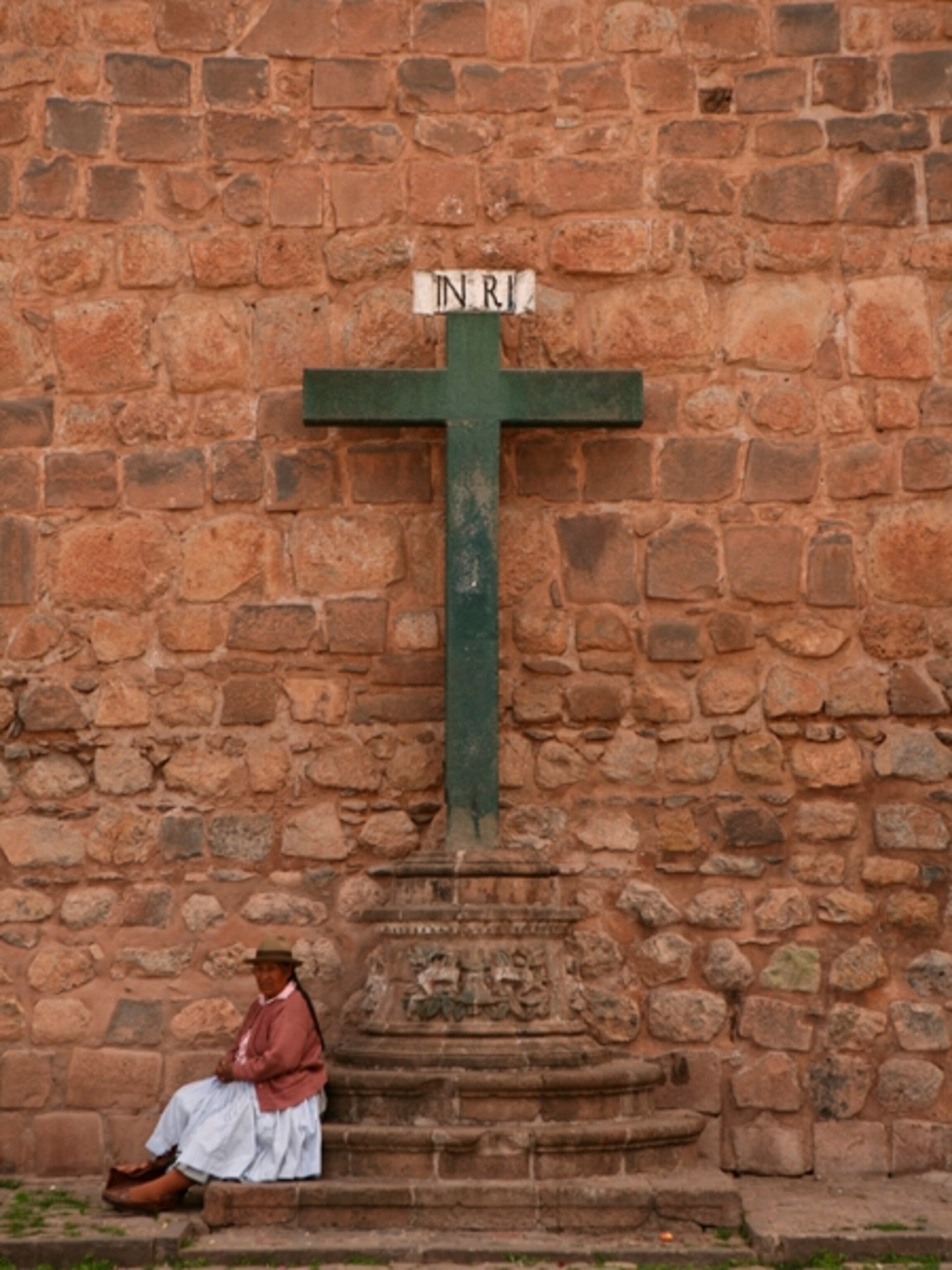 A woman sits beneath a large cross, Cusco, Peru
