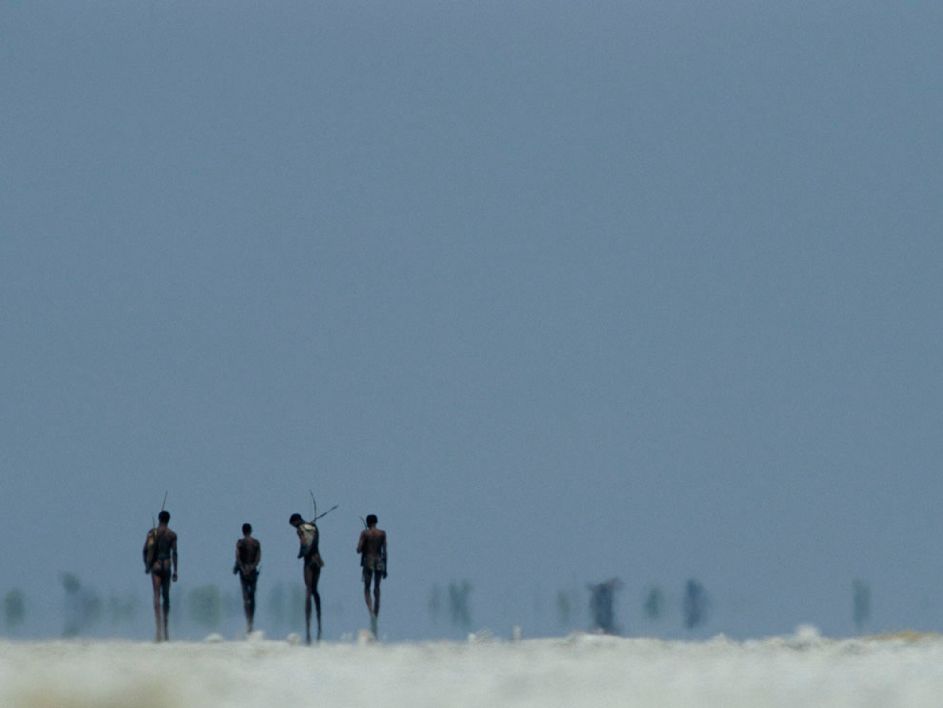 A group of bushmen appears in silhouette, walking across a white salt pan